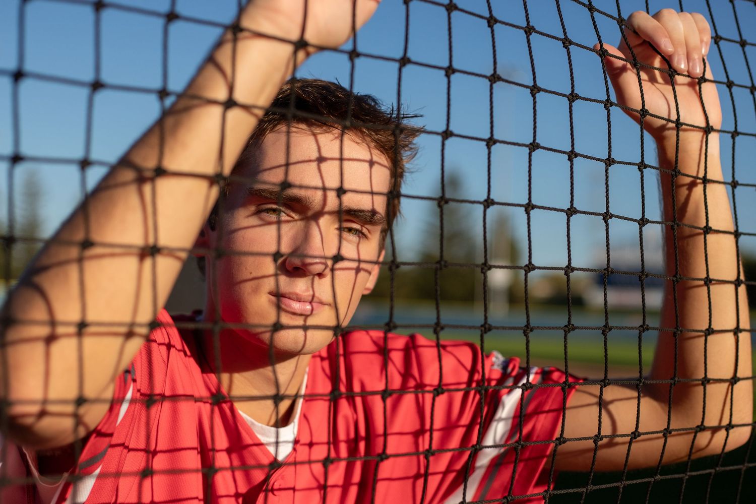 shakopee-mn-high-school-senior-amanda-meier-photography-baseball-player-through-net-behind-home-plate-shadows-on-players-face.jpg