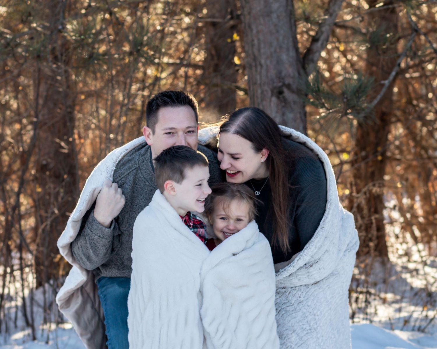 A family shares joyful moments together in a snowy winter forest setting during a photo session.