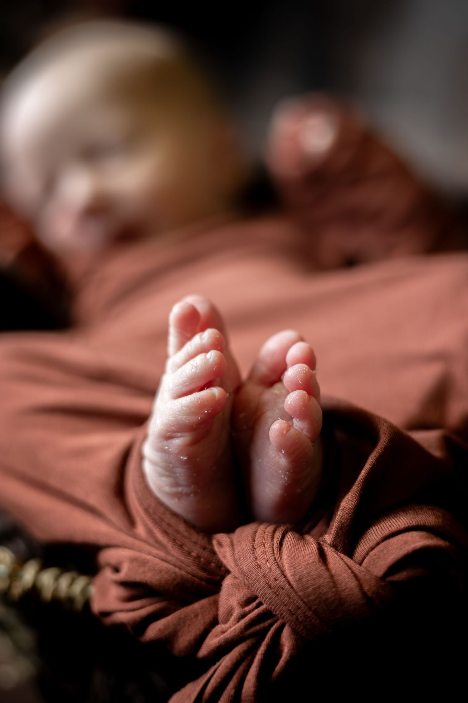 Macro photography sequence showing tiny baby toes emerging from soft brown fabric in dramatic lighting.