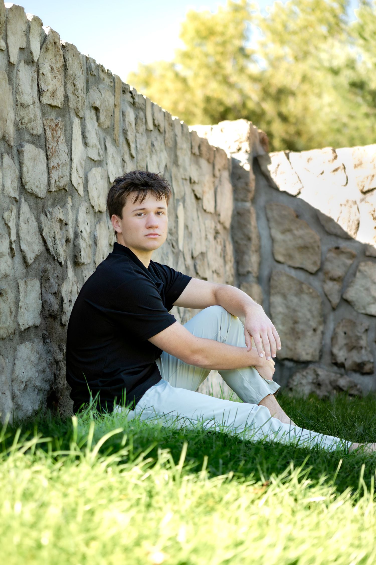 Casual portrait series against a stone wall in grass during golden hour.