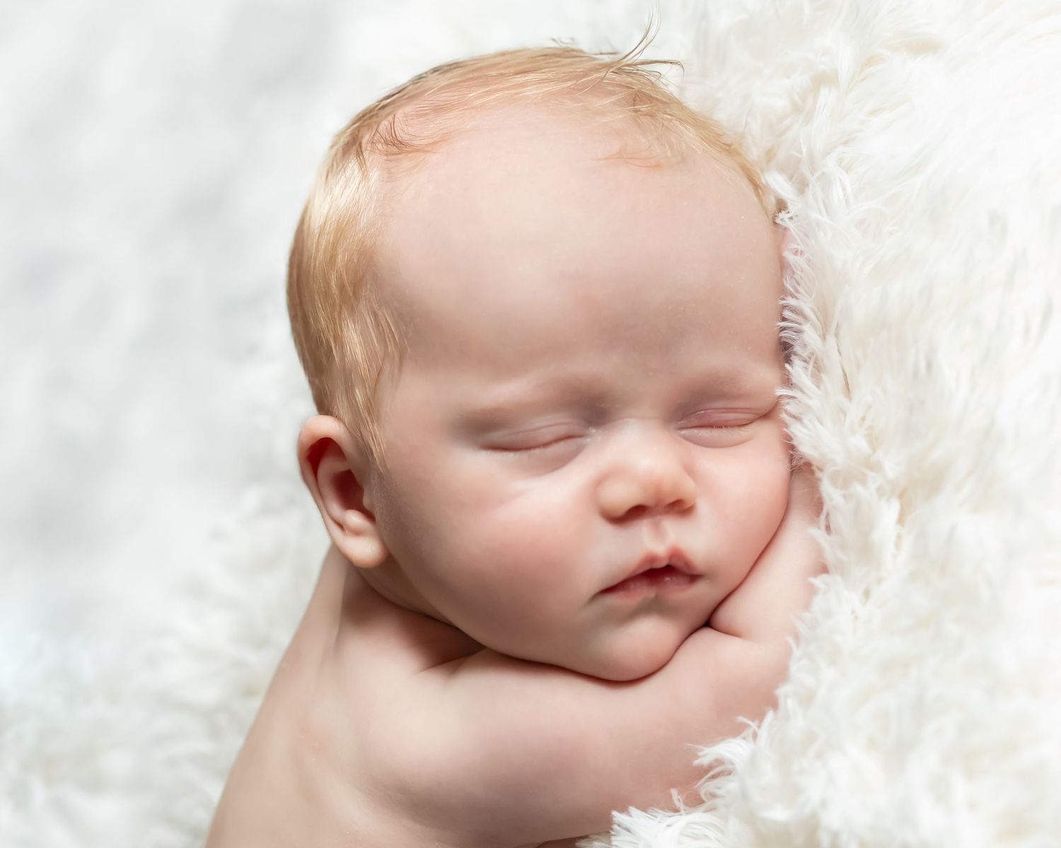 Peaceful sleeping newborn baby rests on soft white blanket in gentle natural light.