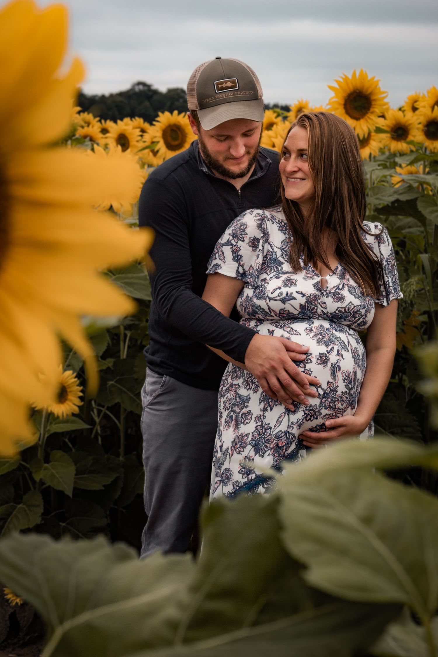 sunflower field maternity session, mom is looking at dad, dad is looking at baby bump