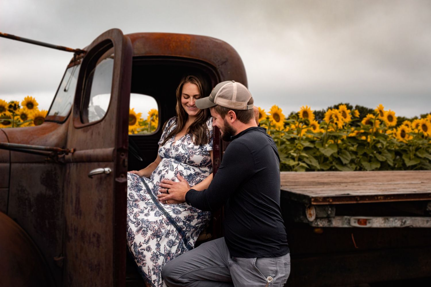 sunflower field maternity session, mom and dad with vintage pickup truck smiling about baby bump