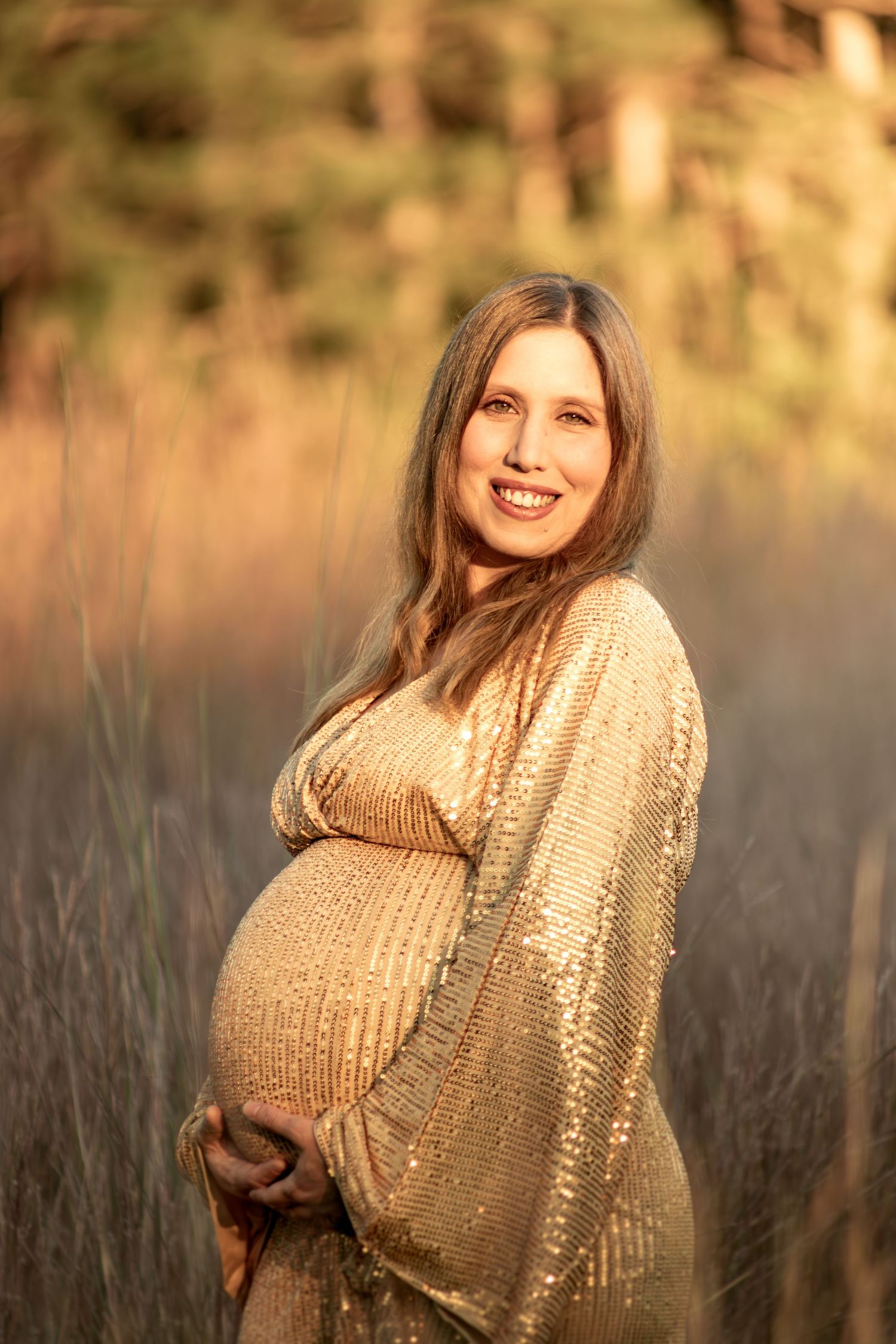 Maternity portrait of expectant mother in sparkling gold dress at sunset.