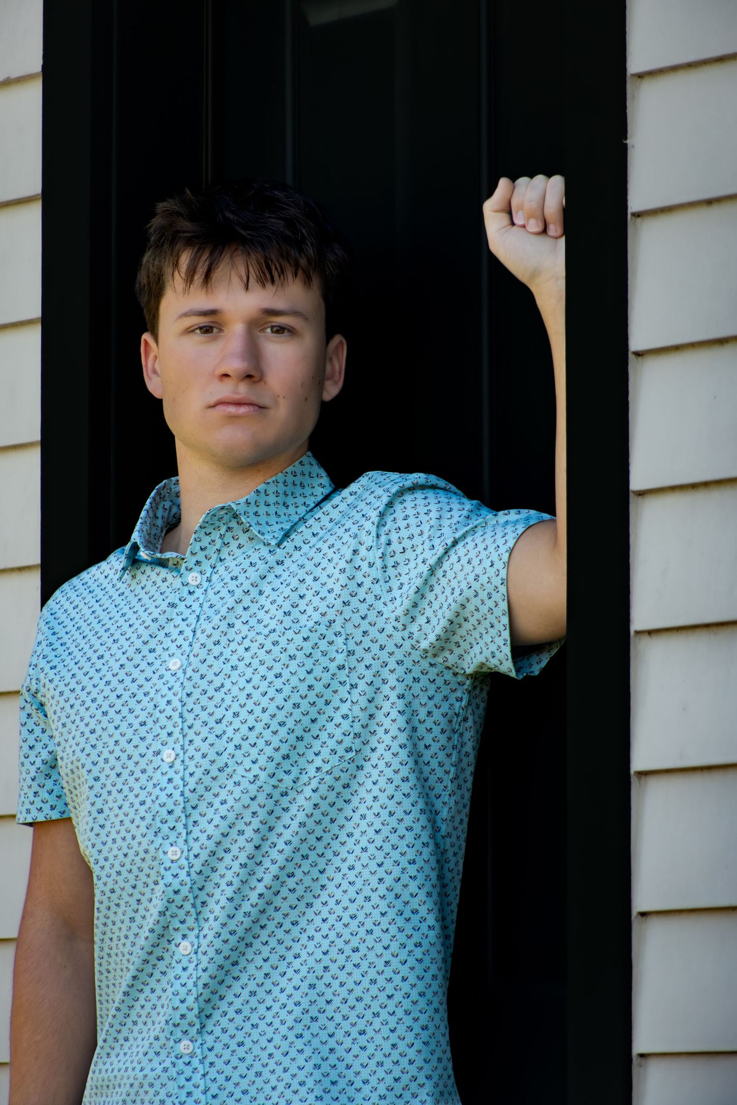 Portrait series against dark siding wearing a blue patterned shirt.