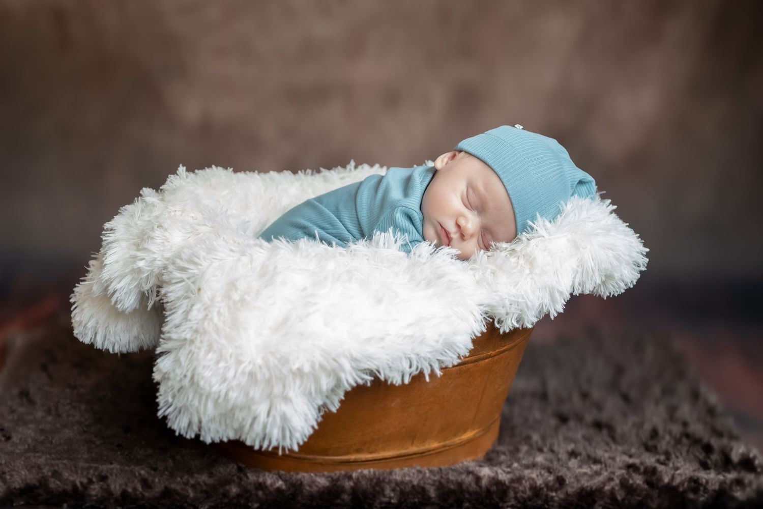 Newborn baby's feet wearing brown leather moccasin booties on a white fluffy blanket.
