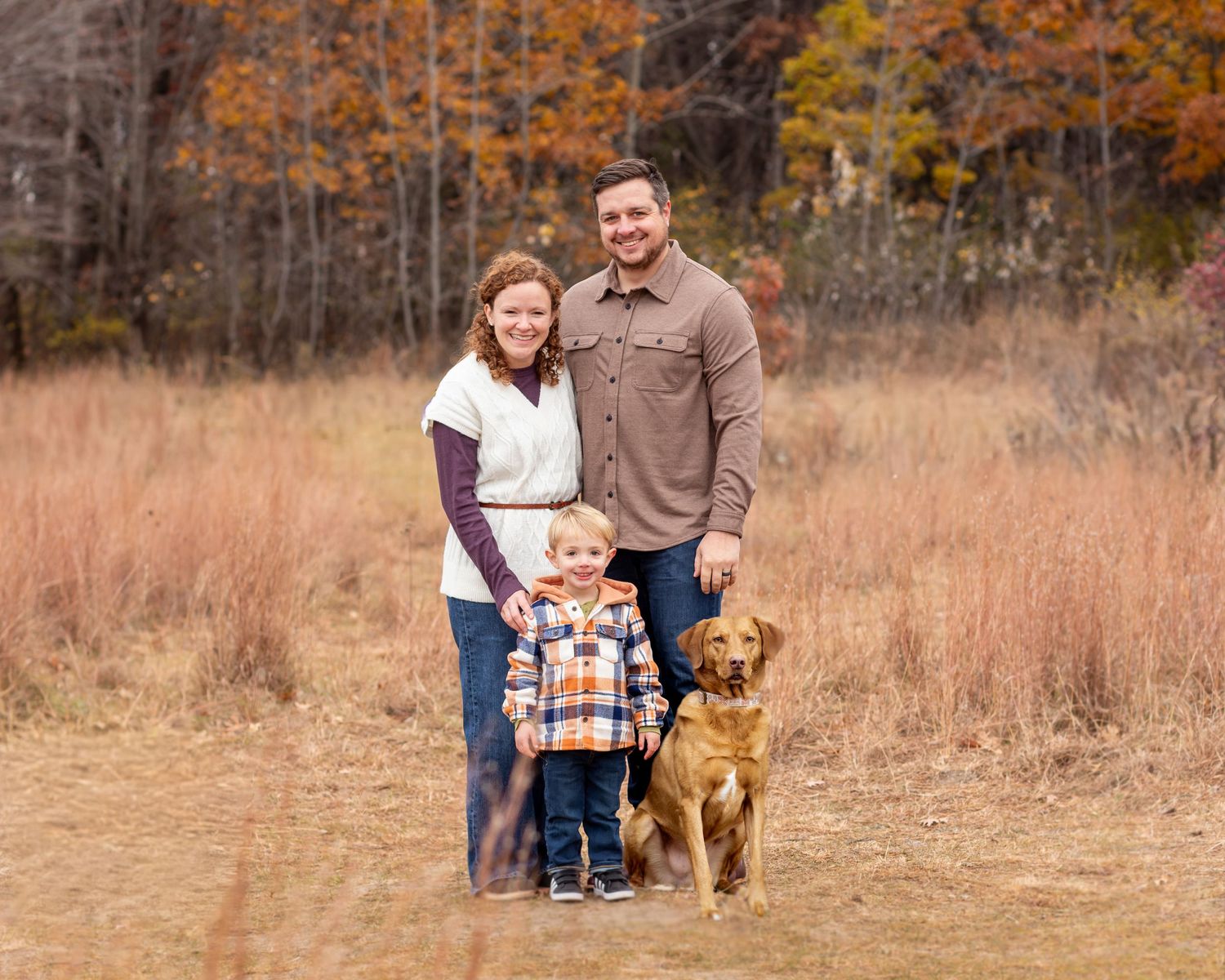 A family and their golden retriever dog pose together in a rustic autumn field during a photoshoot session.