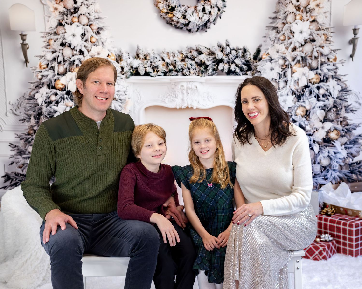 Family poses together in front of flocked Christmas trees and holiday decorations for a festive portrait.