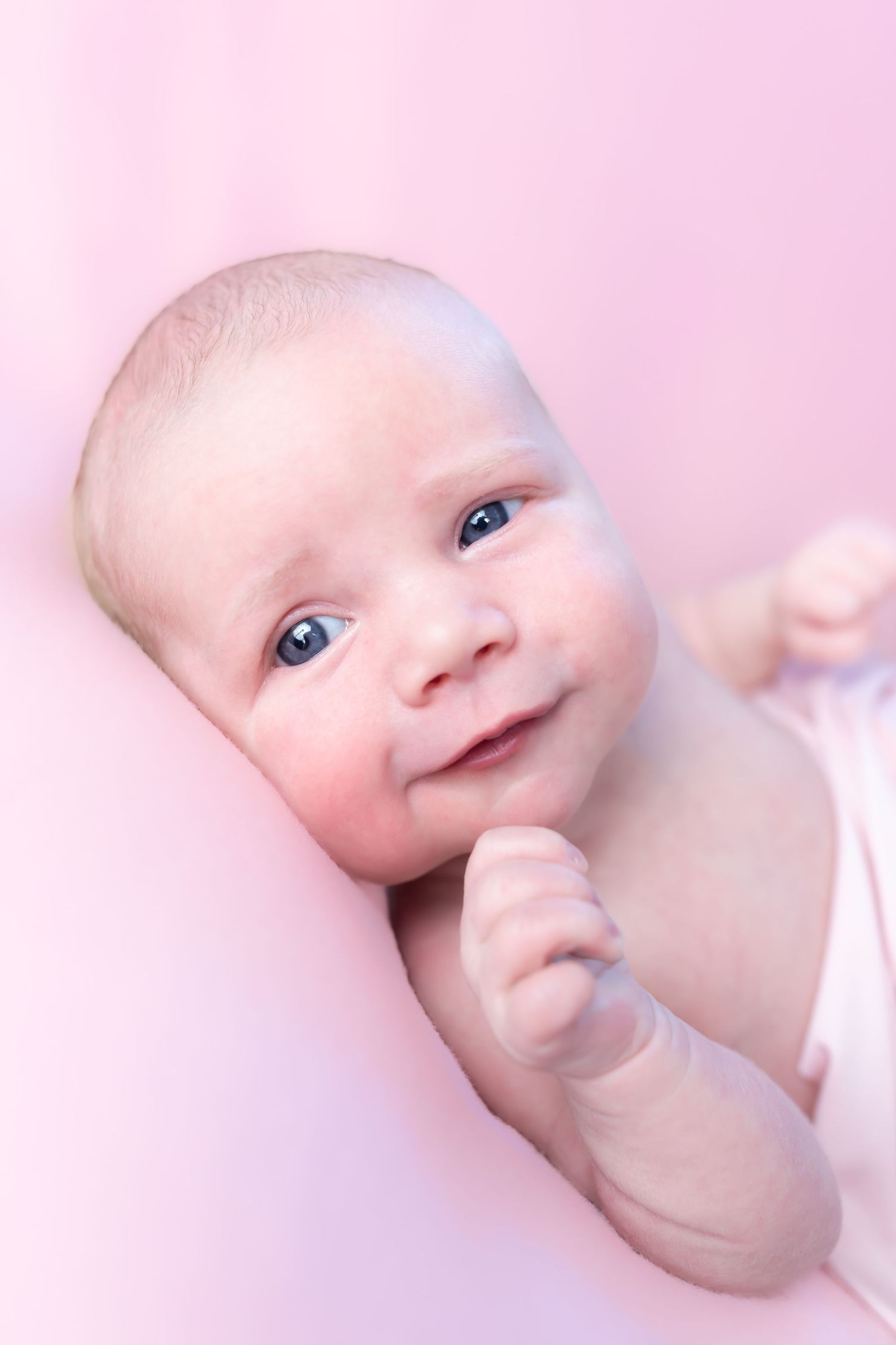 Close up portrait of an infant with bright blue eyes against a soft pink background.