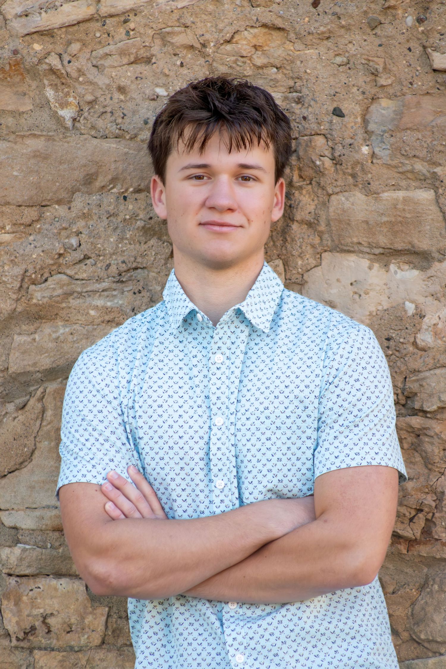 Portrait series against textured stone wall wearing light blue shirt.