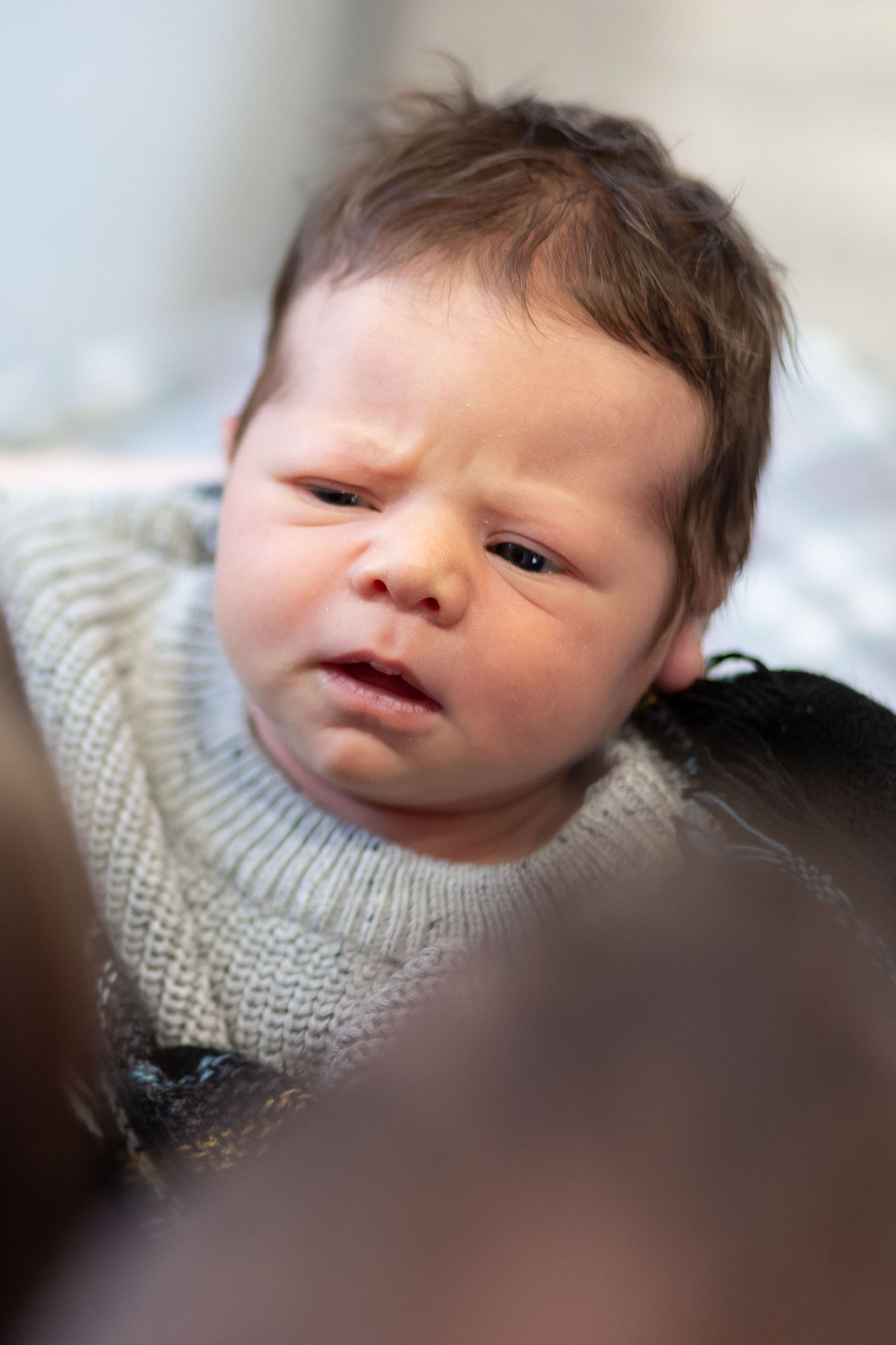 A newborn baby wearing a white knit sweater is shown in a series of soft-focus close-up portraits.