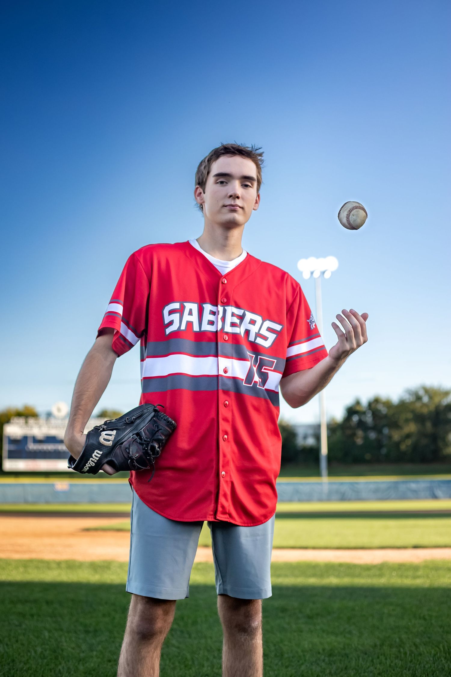 shakopee-mn-high-school-senior-photography-baseball-player-lights-on-in-background-tossing-ball.jpg