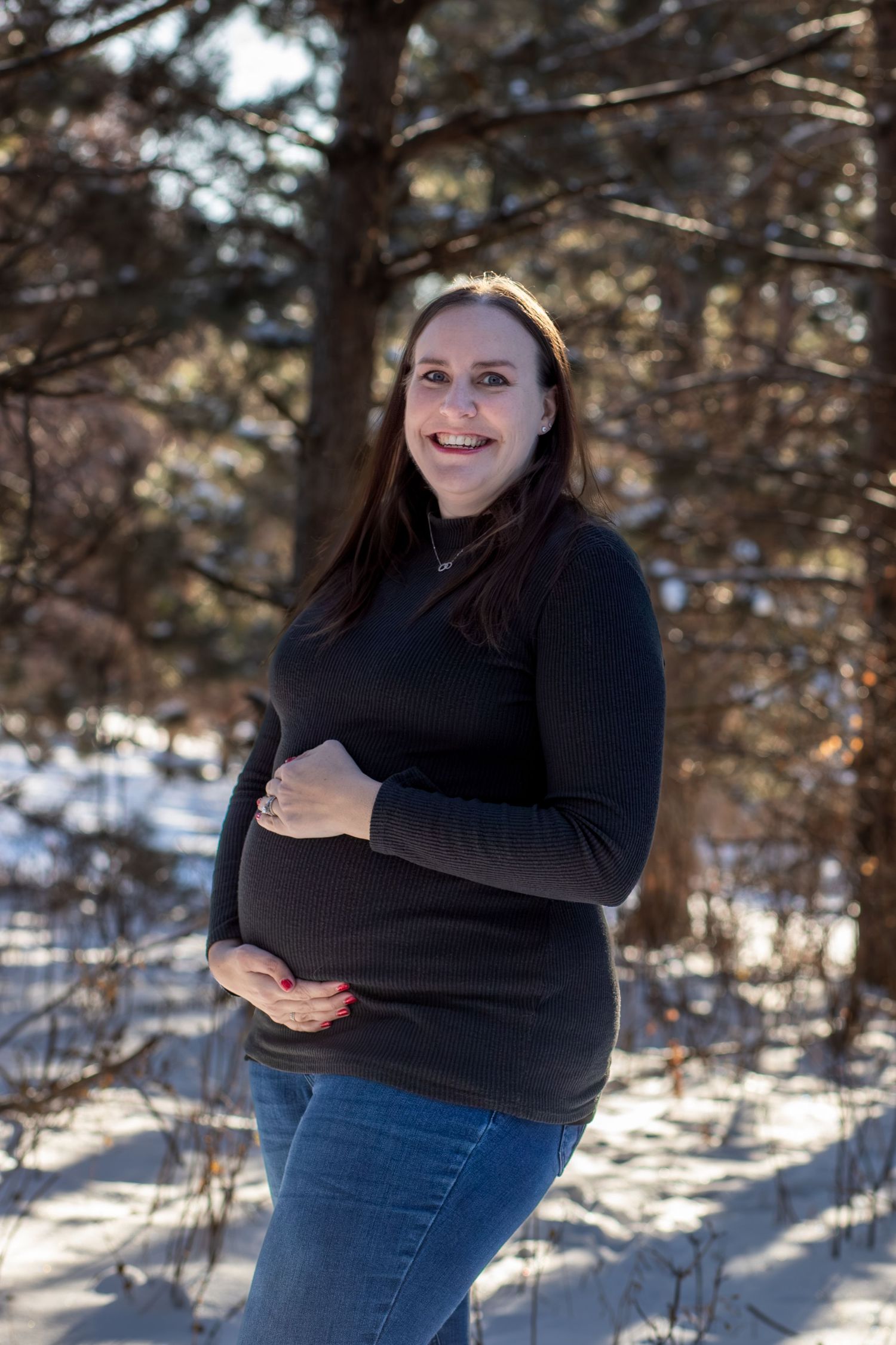A series of winter maternity photos showing a woman in a black sweater and jeans posing against a snowy forest backdrop.