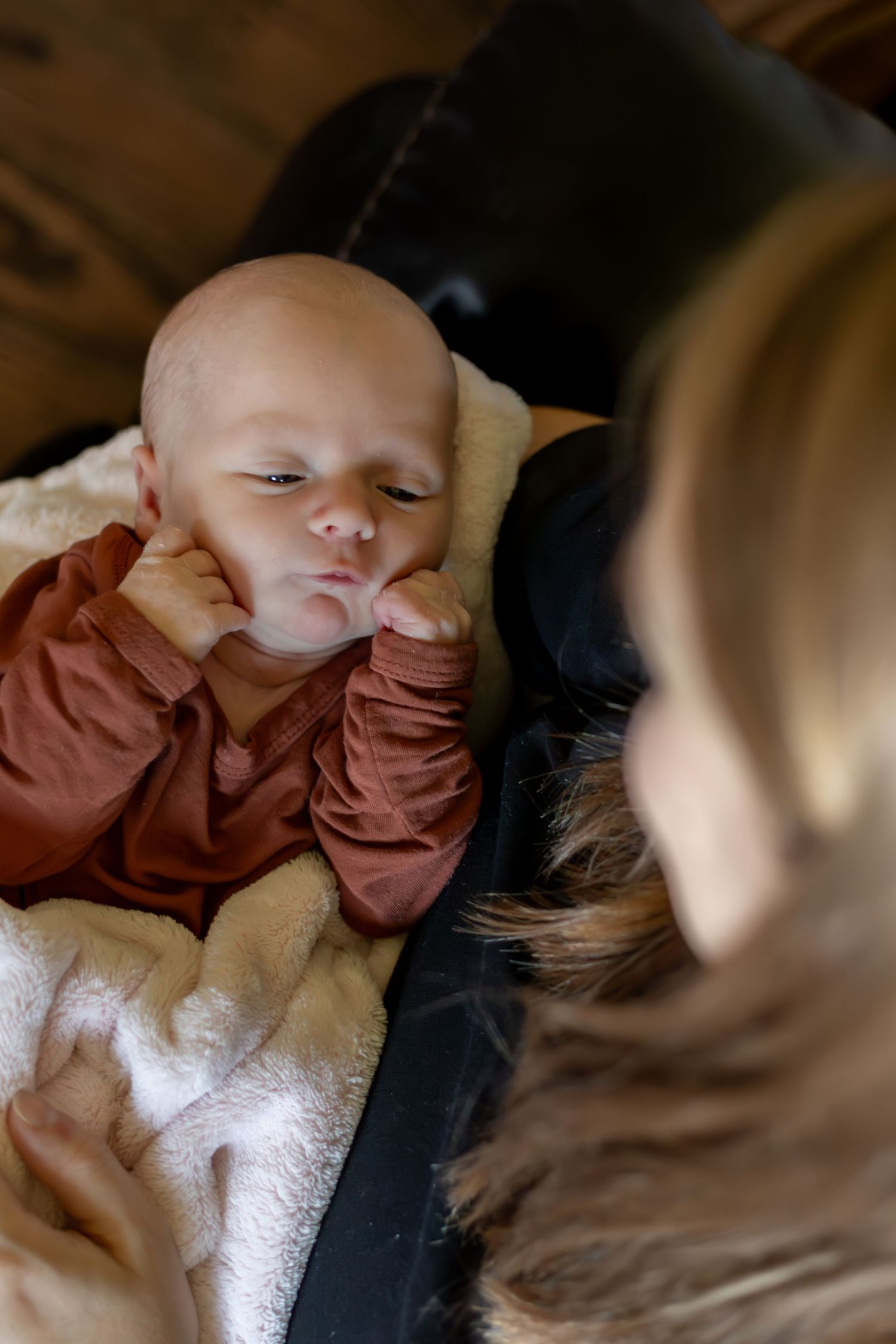 A sleeping baby wearing a brown outfit rests peacefully on a white blanket.