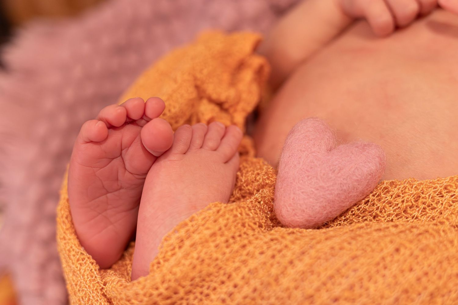 A tiny newborn baby's feet resting on a soft knitted yellow blanket in warm lighting.