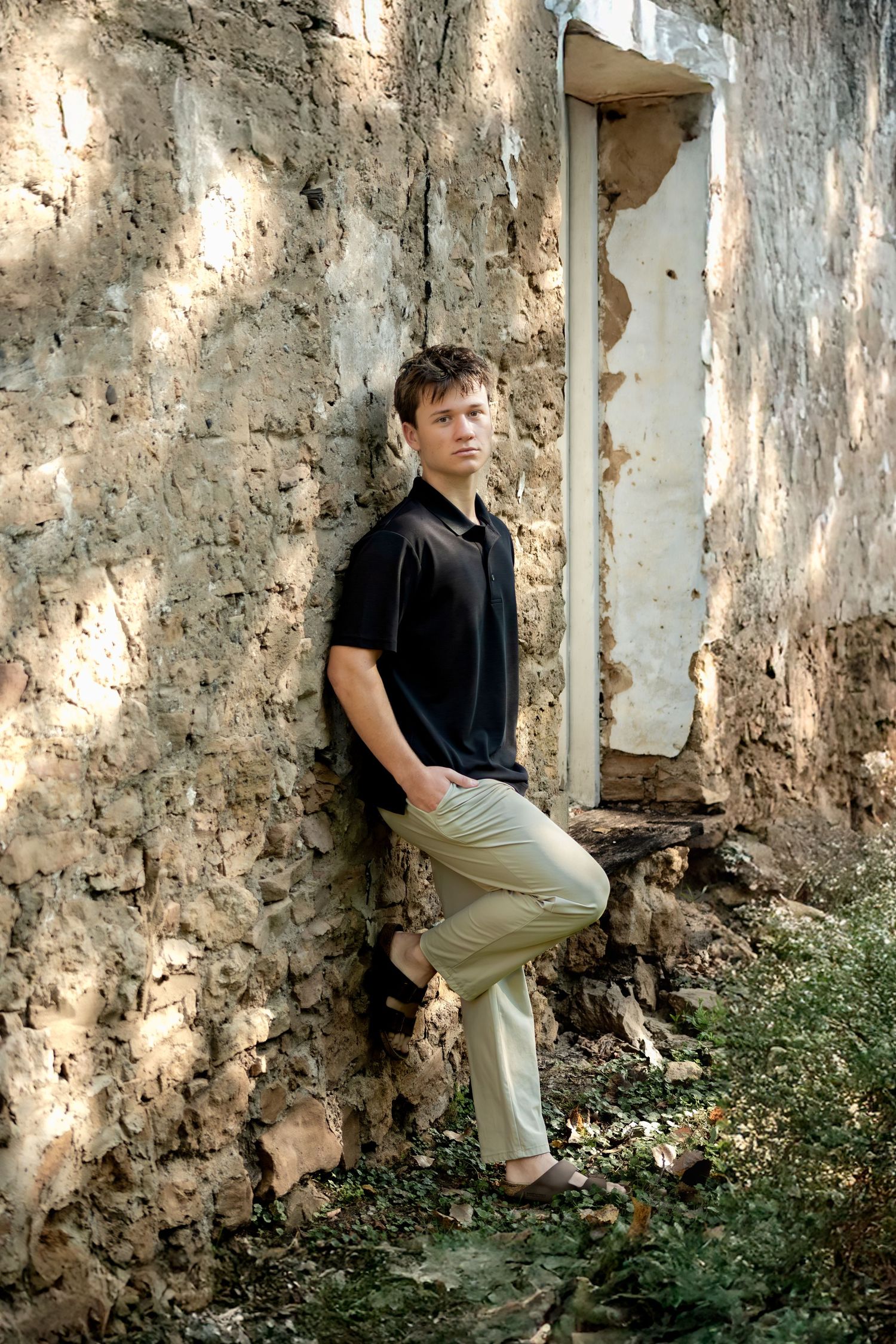 Portrait of person leaning against weathered stone wall in natural lighting.