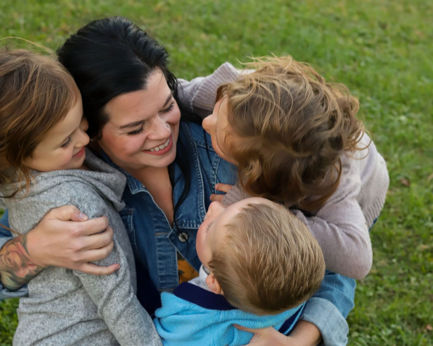 A loving family embraces outdoors on green grass in a series of candid moments.