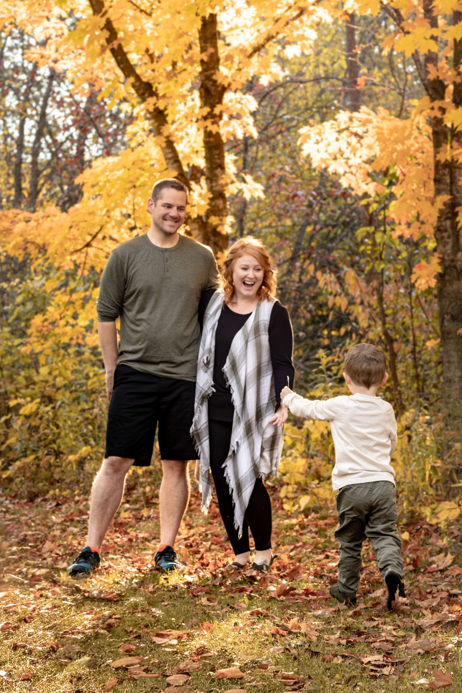 Energetic family playing in fallen autumn leaves during outdoor photoshoot.