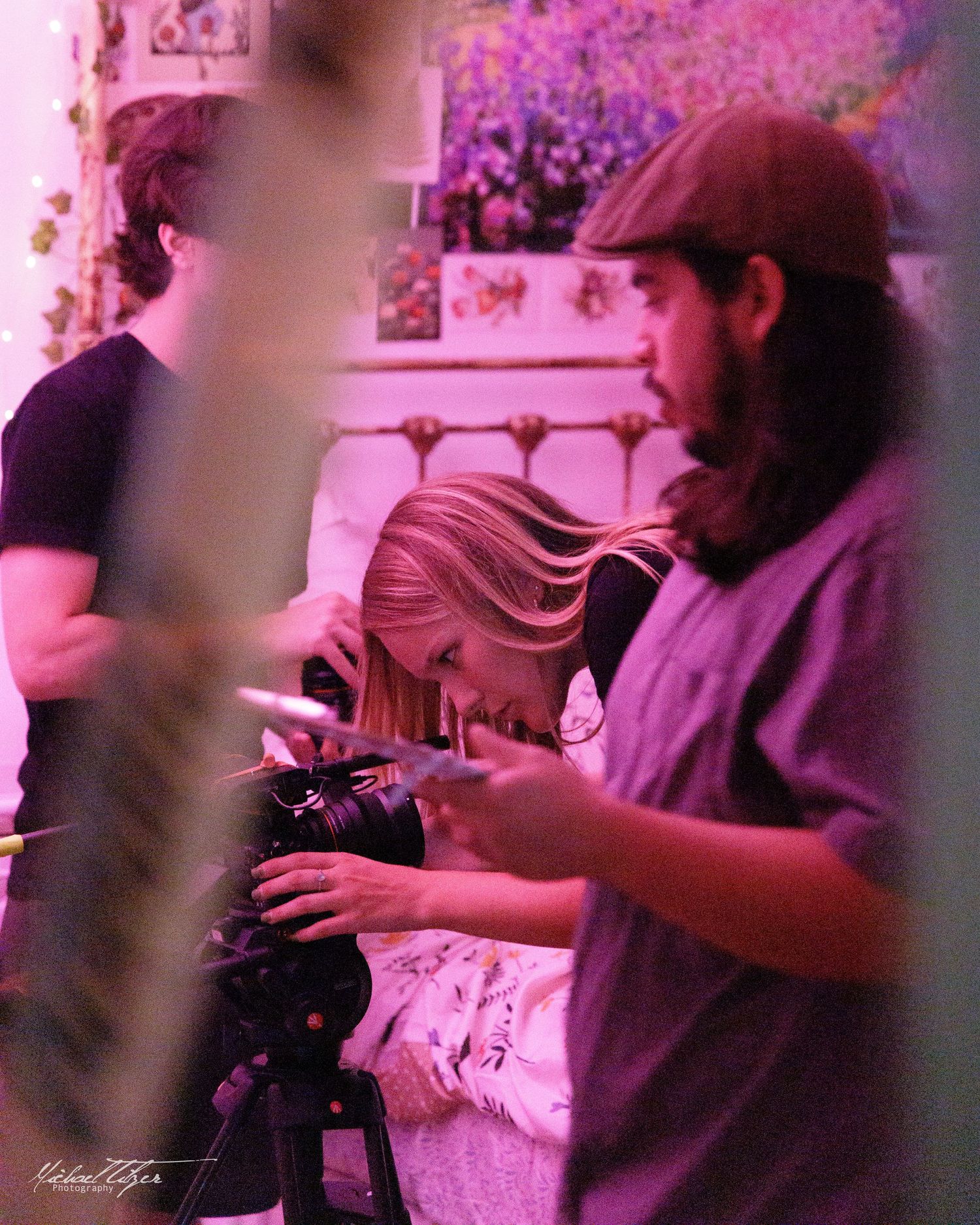 Behind the scenes filming in a pink-lit room with production crew and equipment.