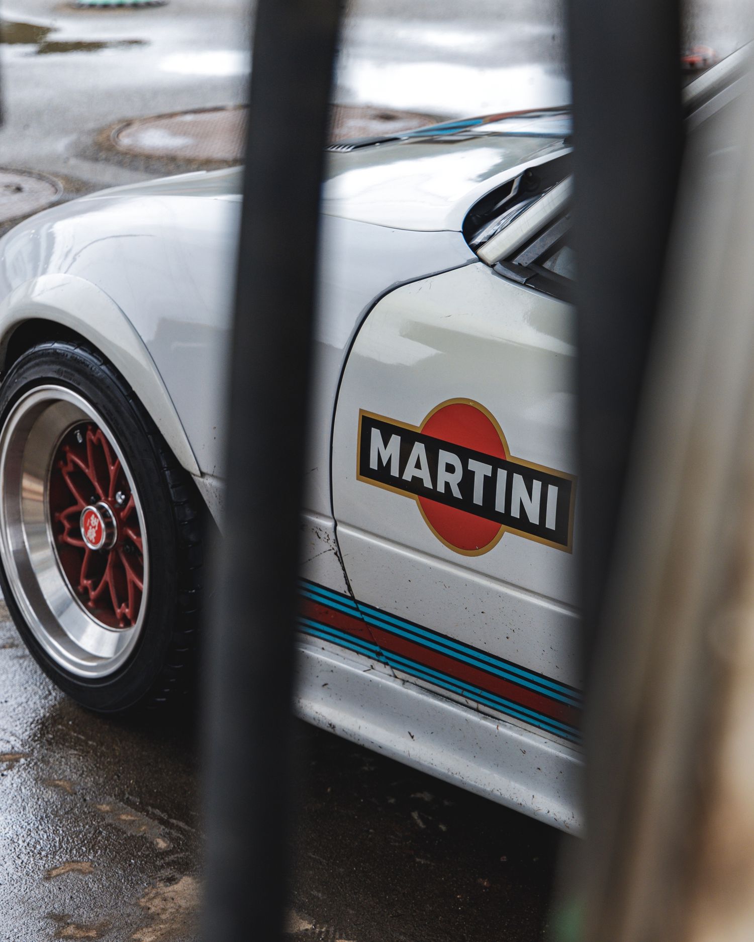 White Martini-branded race car viewed through vertical bars with red racing wheels visible.