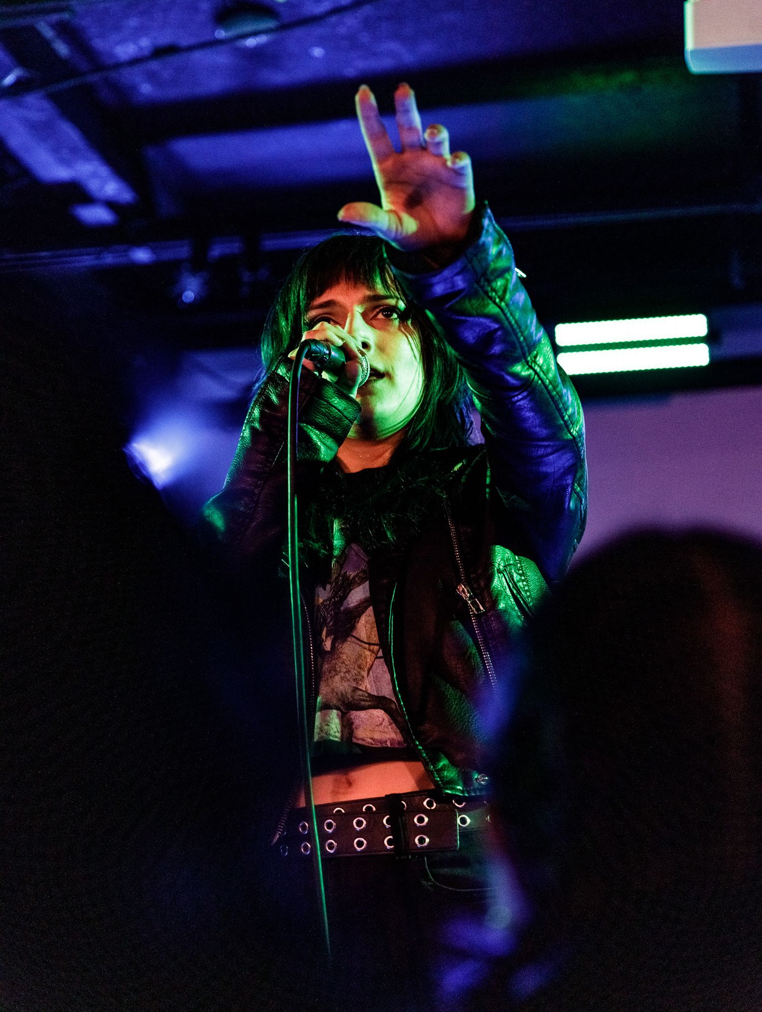 Concert performer sings passionately under dramatic blue and green stage lighting.