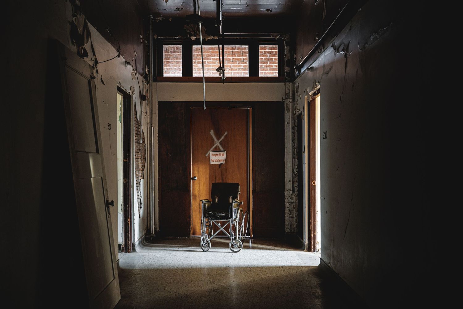 Dark corridor in abandoned building with light filtering through doorway at the end.