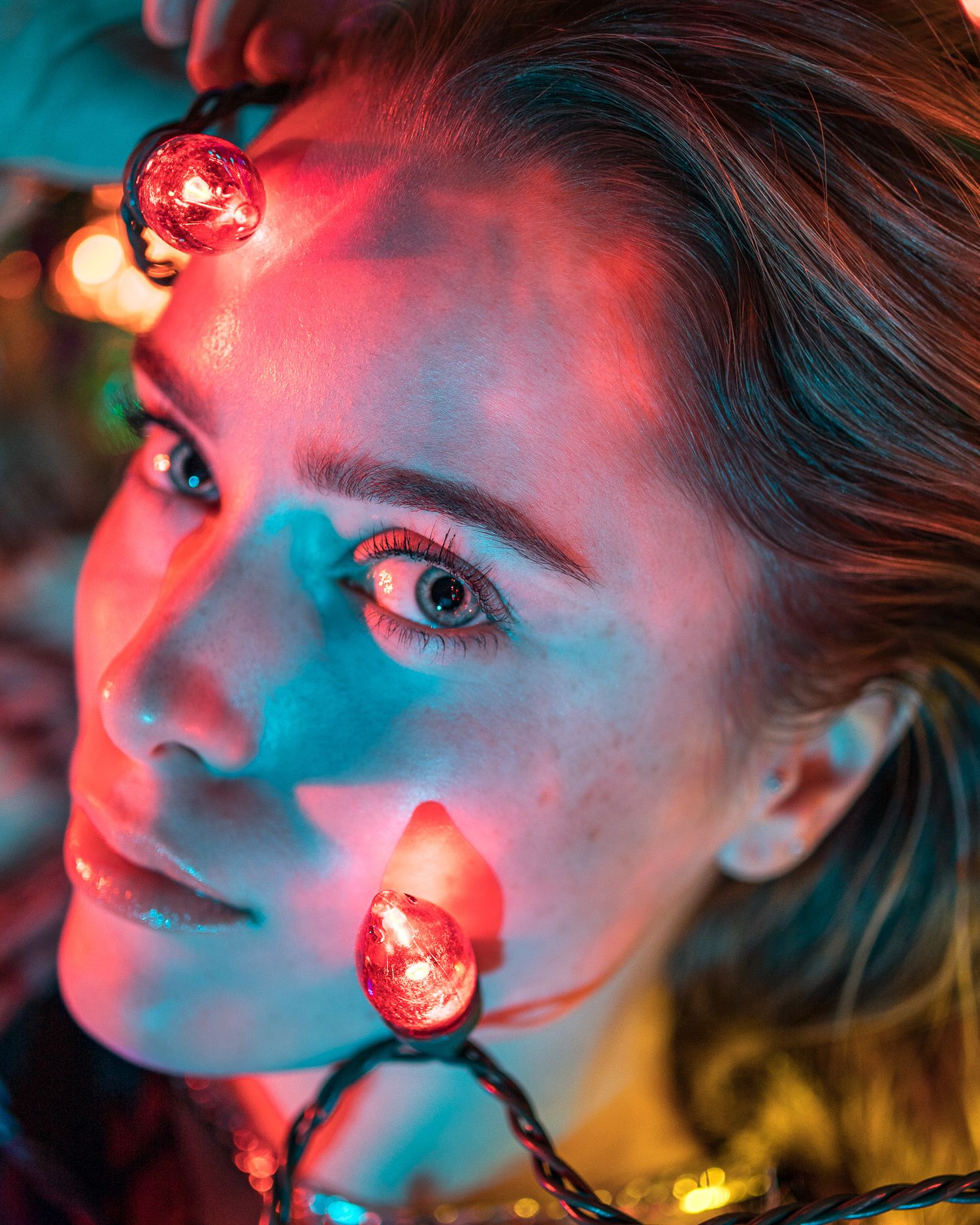 Close-up portrait illuminated by colorful Christmas lights creating magical effect.