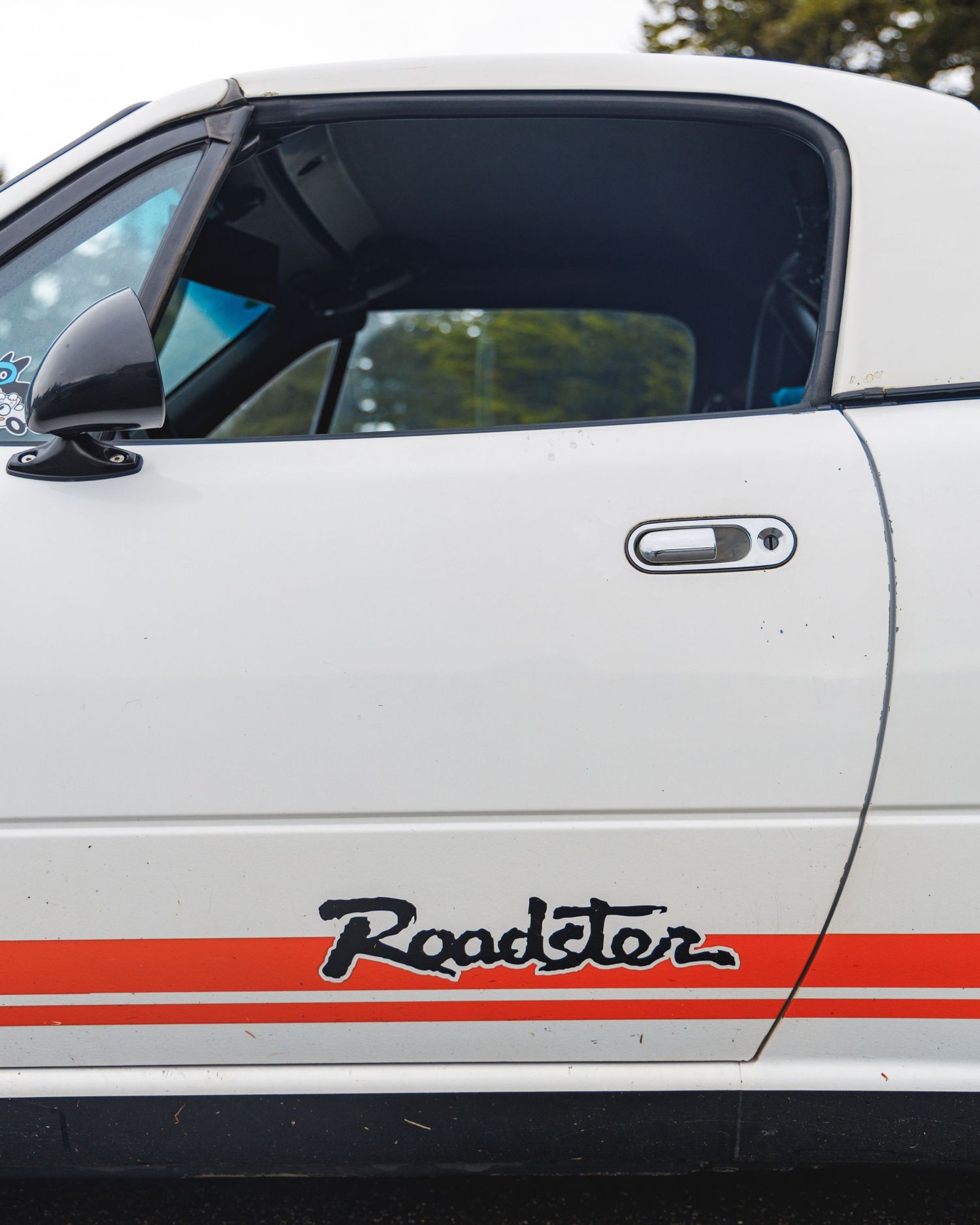 Close-up view of a white classic car with red racing stripes and Roadster lettering on the side panel.