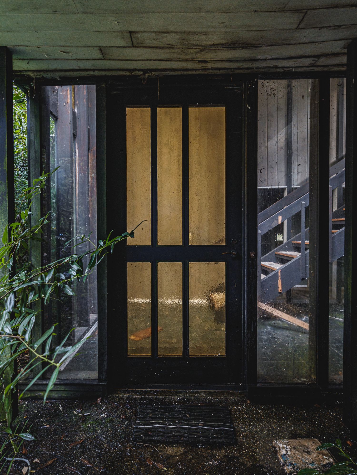Dark interior of an abandoned building with yellow-lit windows visible through glass panes.