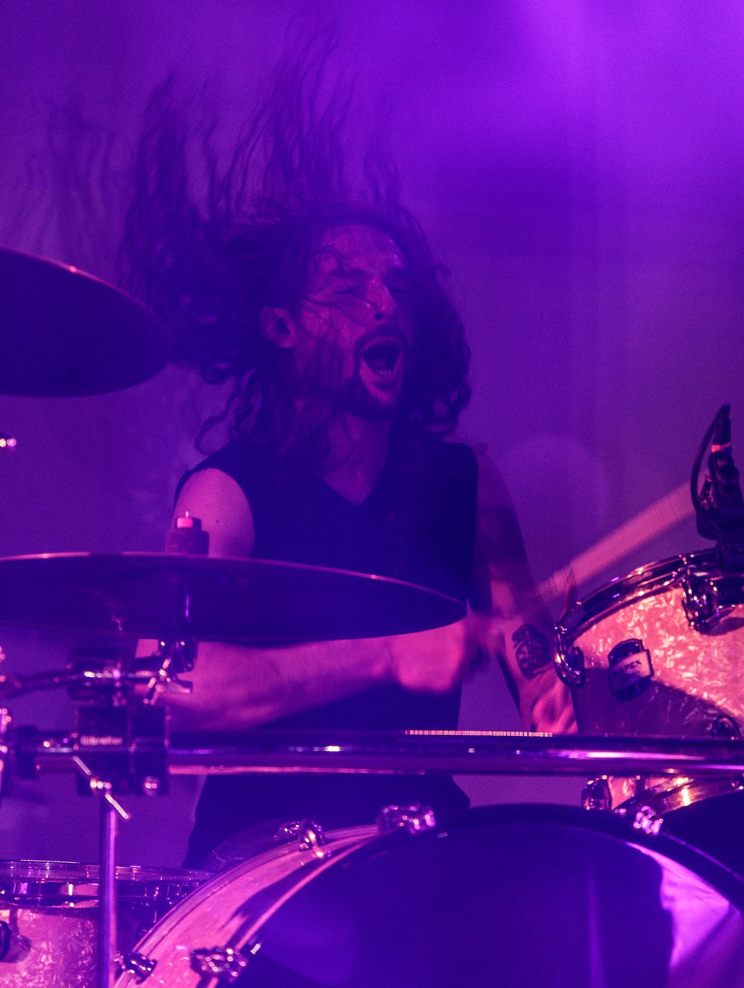 Close-up shots of a drummer performing on stage under purple lighting at a live concert.