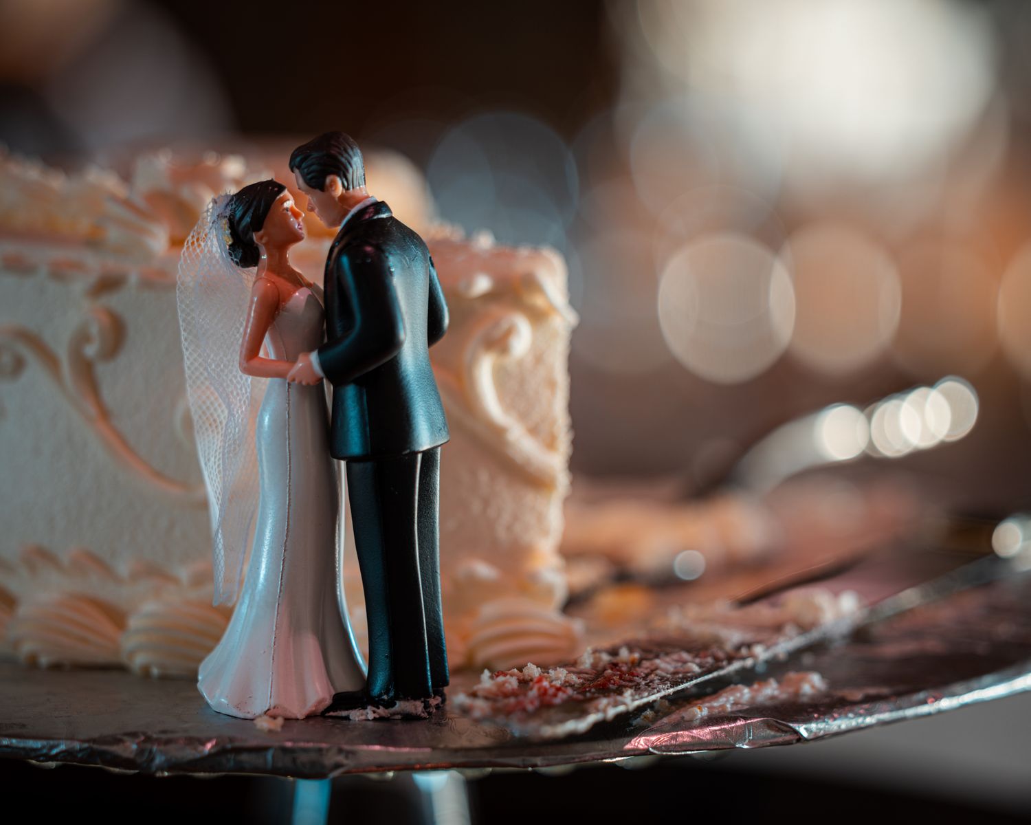 Artistic macro shot of miniature wedding cake toppers with bokeh lighting effects.