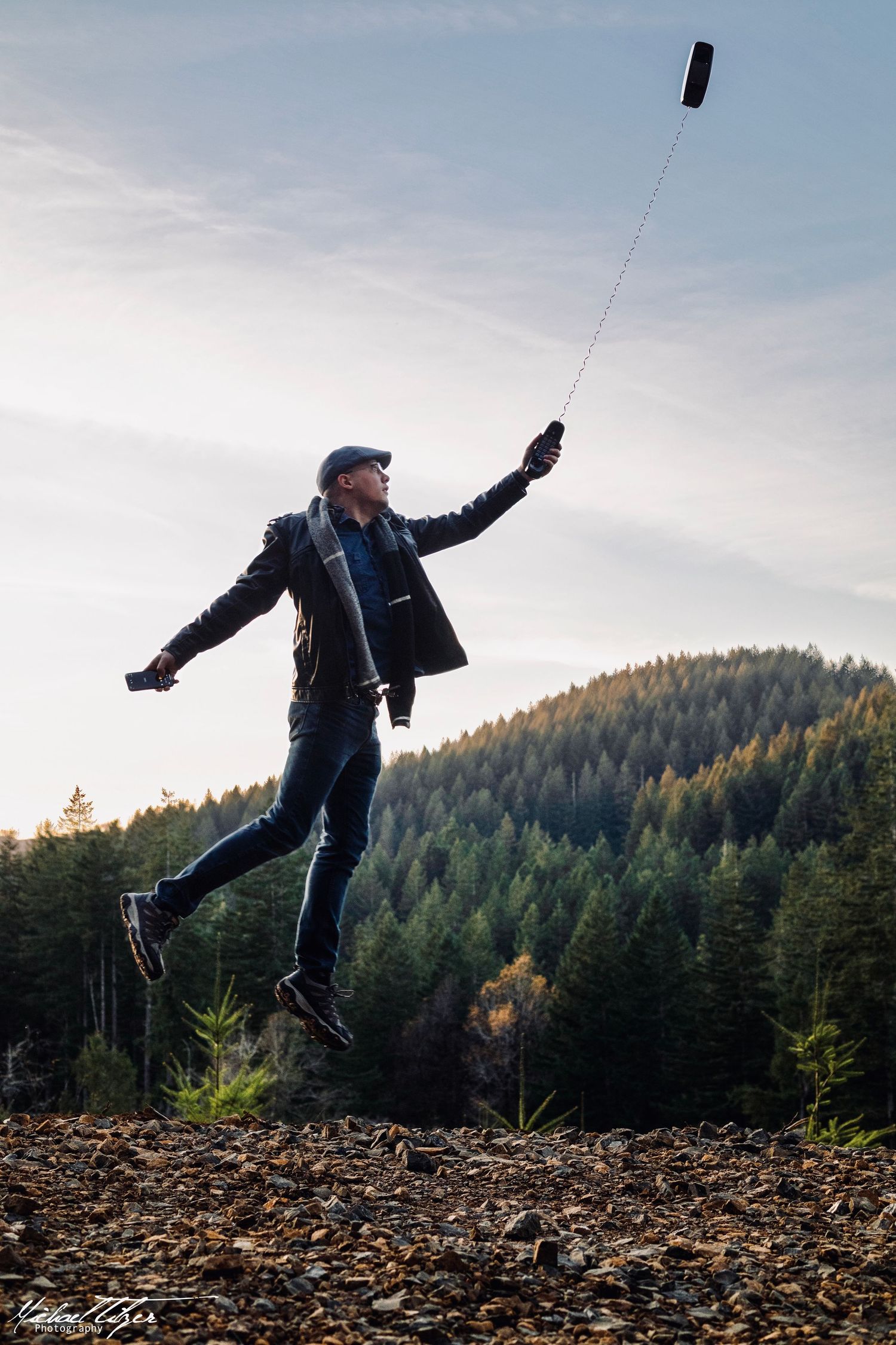 Silhouetted figure leaps dramatically against forested mountain backdrop.