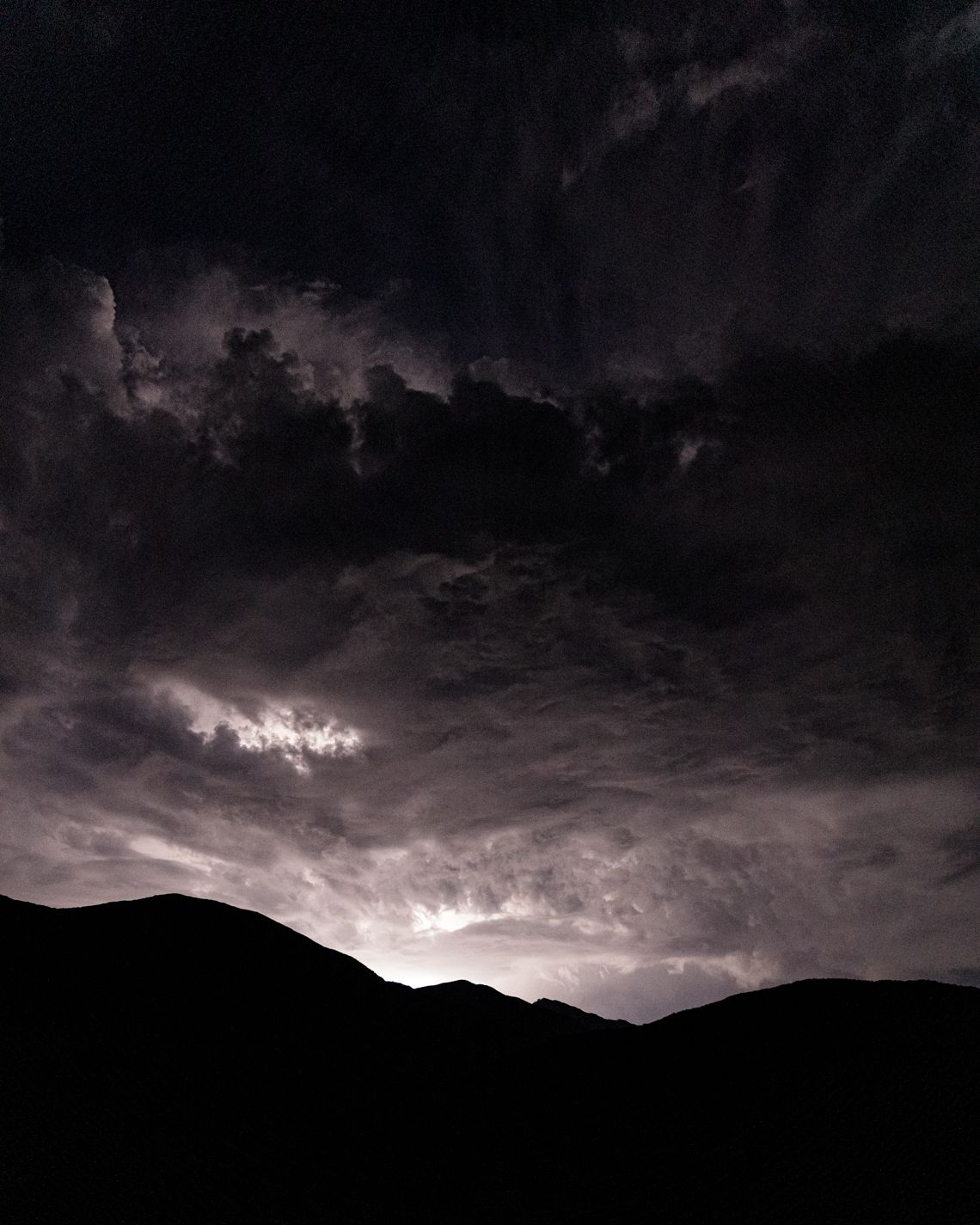 Dark stormy mountain silhouettes under dramatic cloudy night sky.