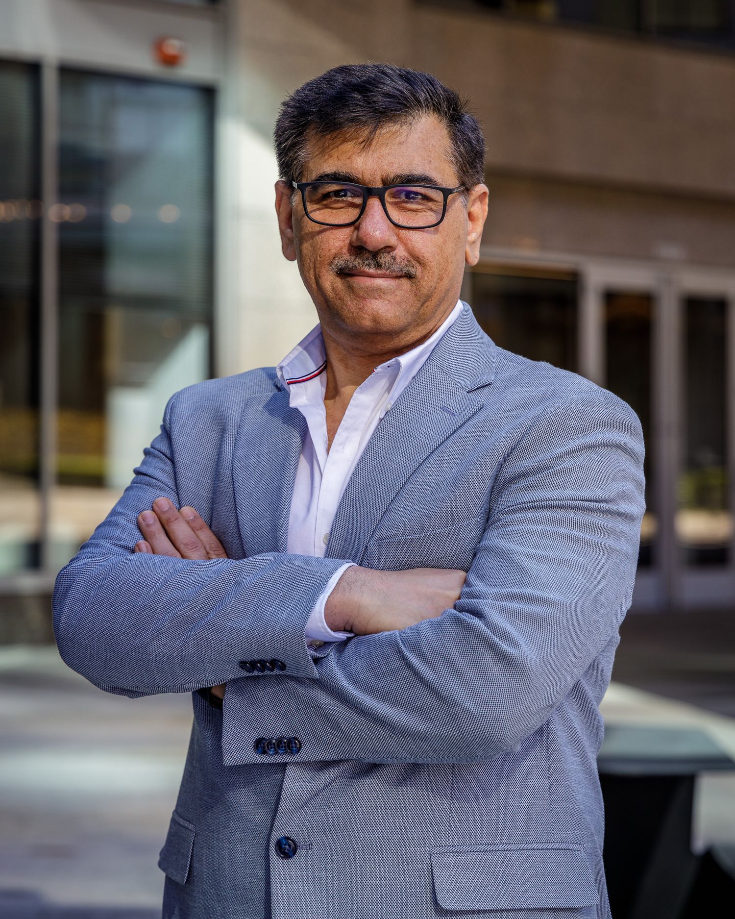 Business professional in a gray suit smiles confidently outside an office building.