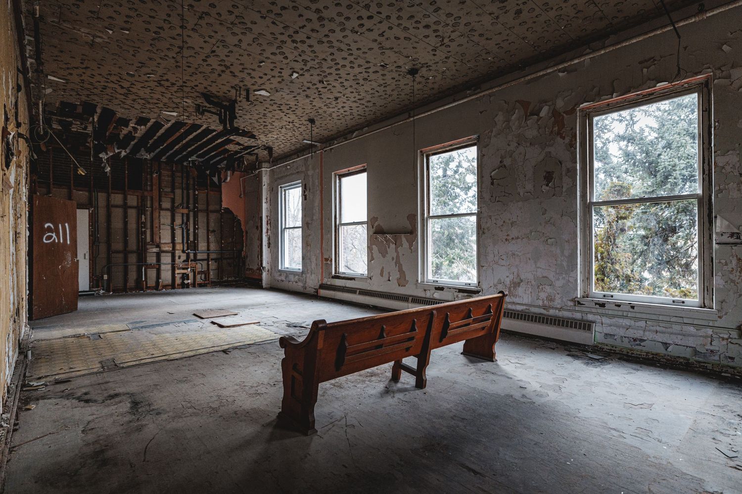 Deteriorating interior room of abandoned building with exposed ceiling beams and broken windows.