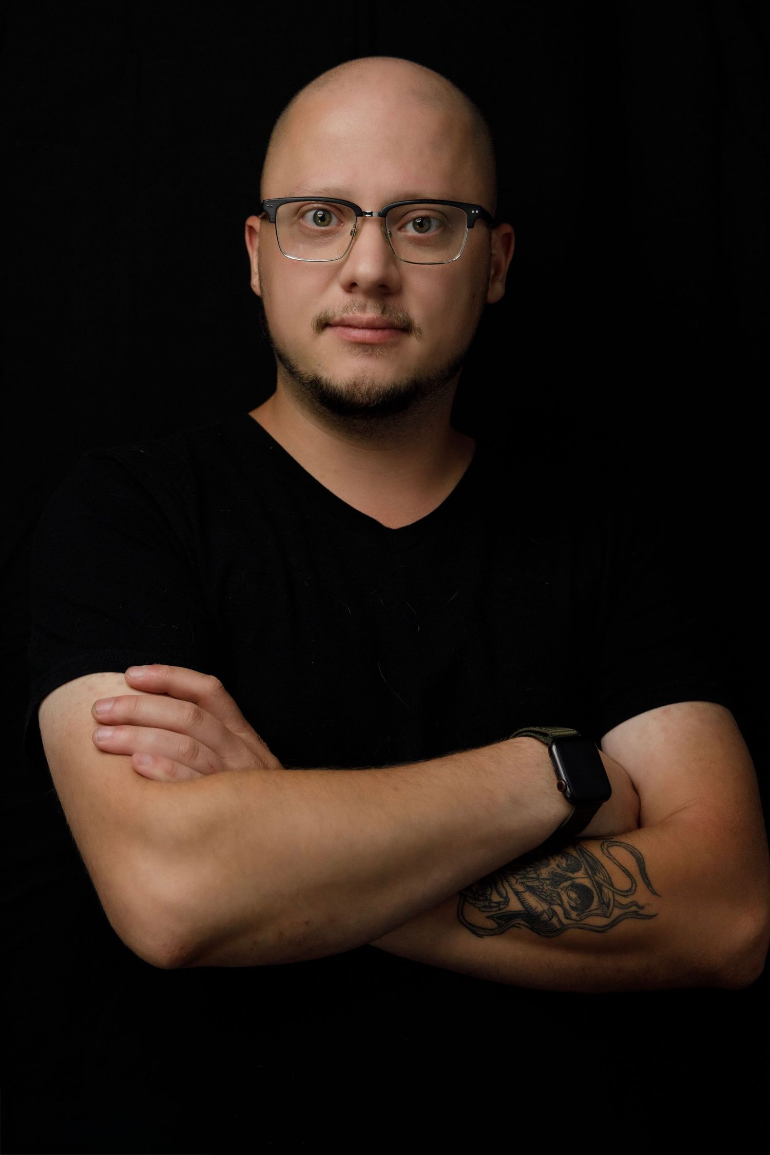 Studio portrait of person in black v-neck with glasses against dark background.