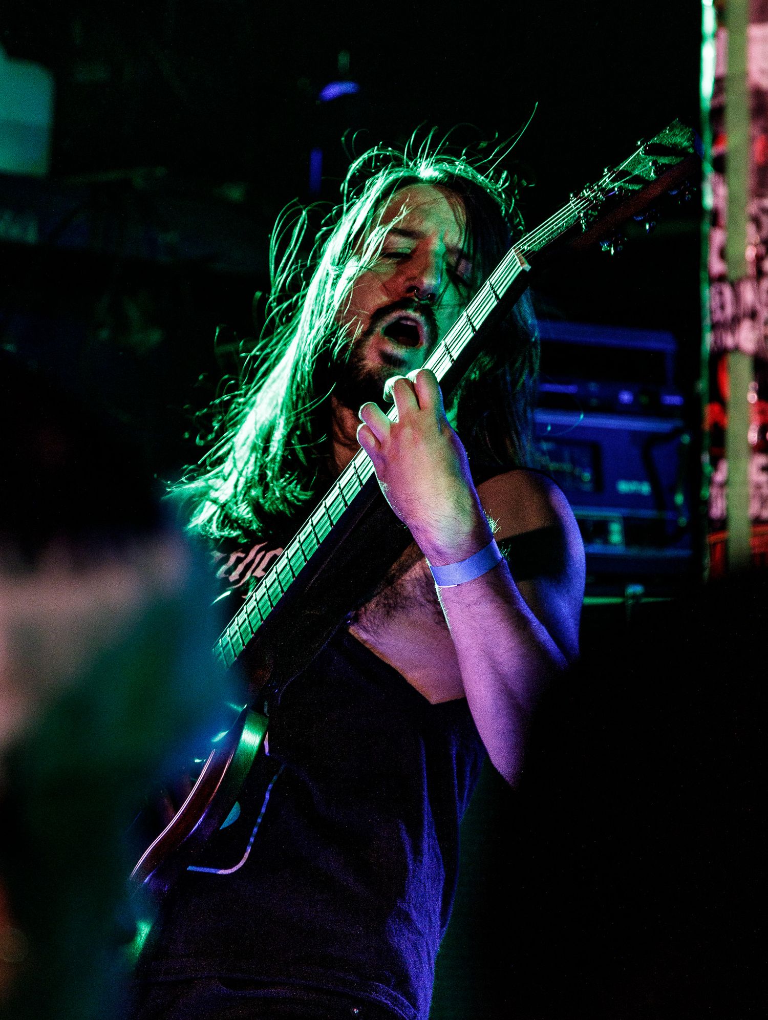 Concert performer sings passionately on stage under dramatic blue and green spotlights.