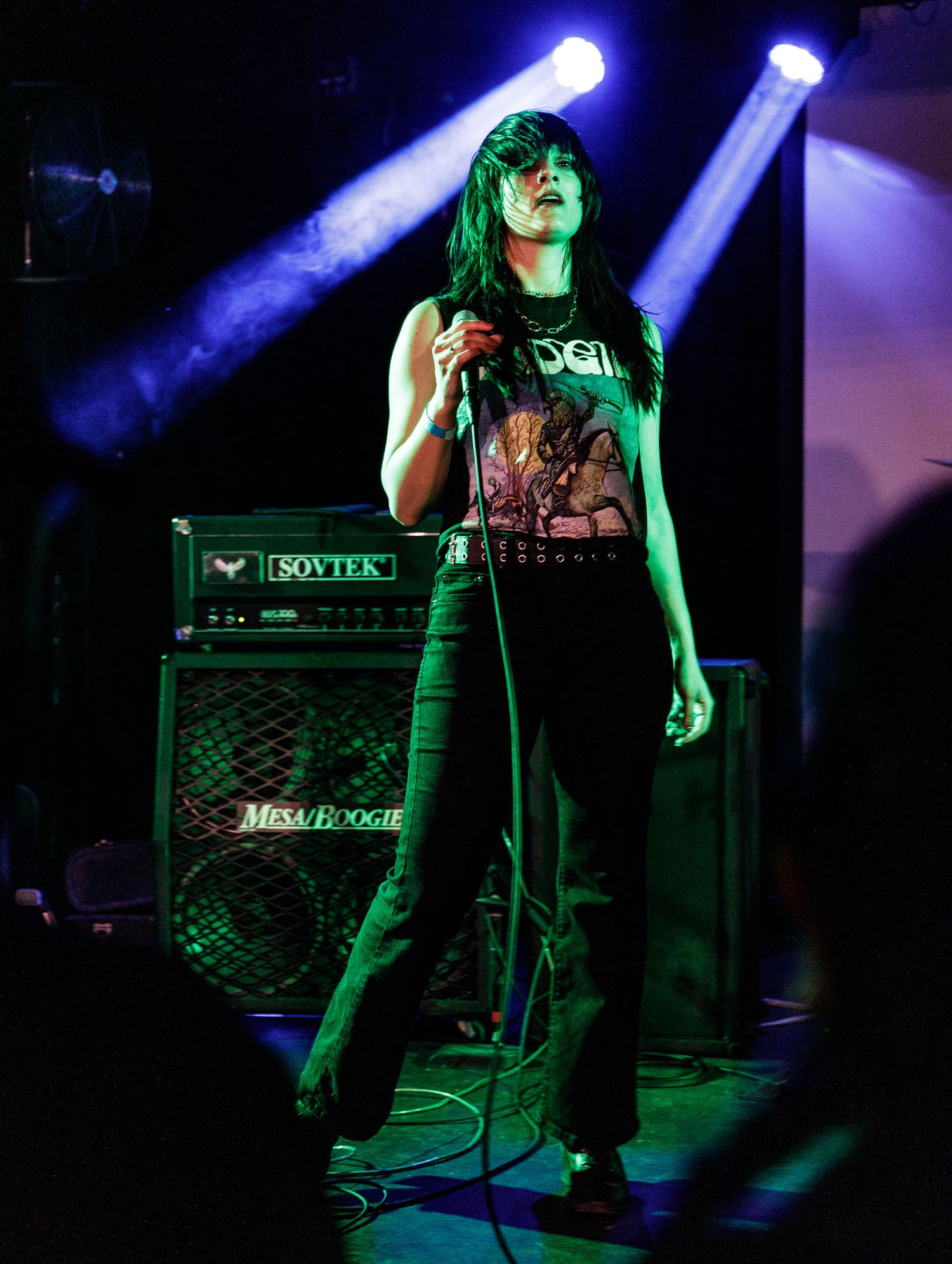 Rock concert with amplifier stack visible on darkened stage under blue spotlights.