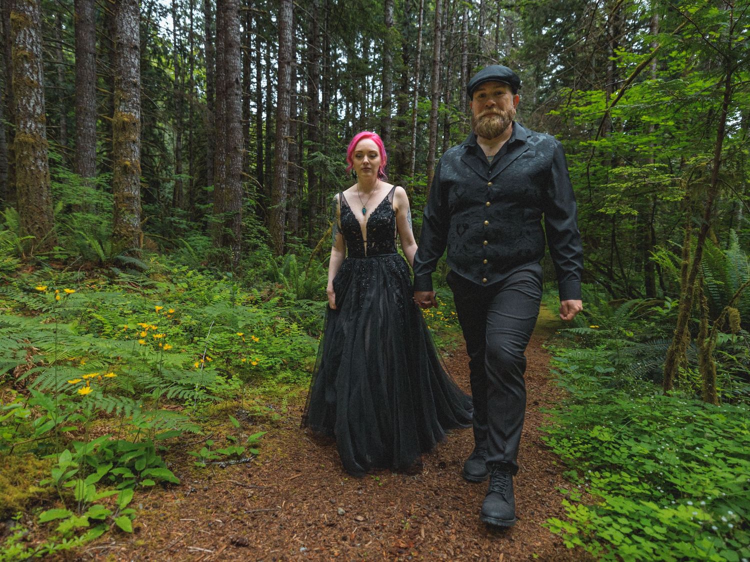 Couple walking along a forest trail surrounded by lush green vegetation.