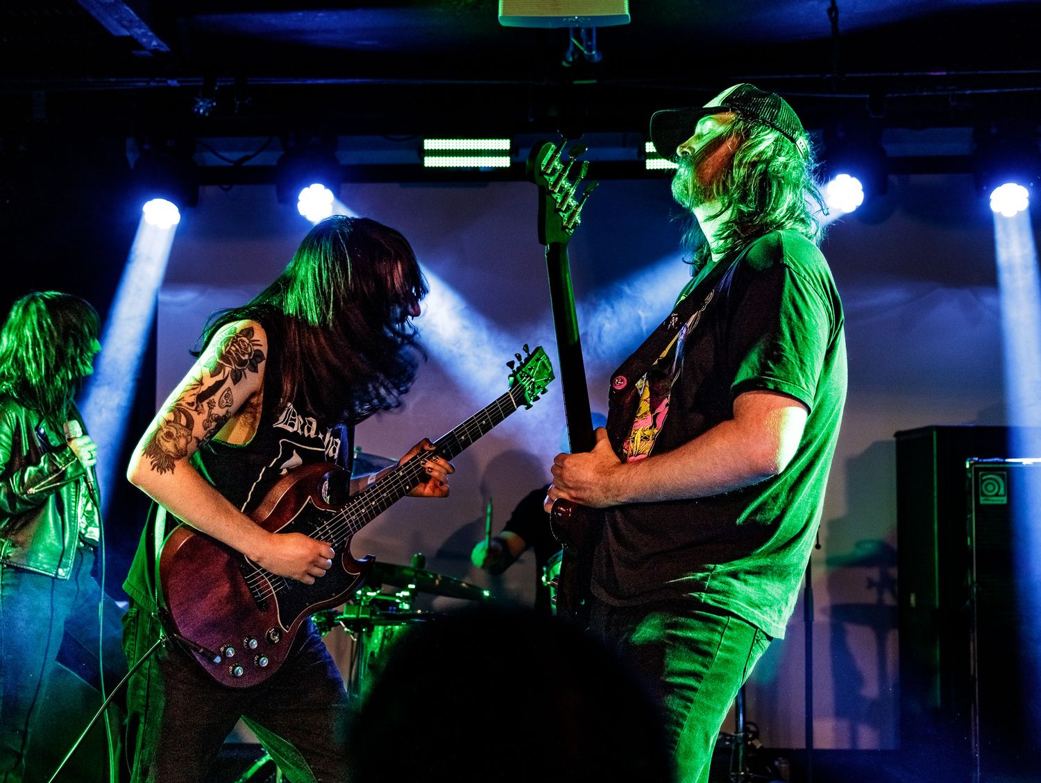 Rock band performs energetically on stage with dramatic blue and green lighting effects.