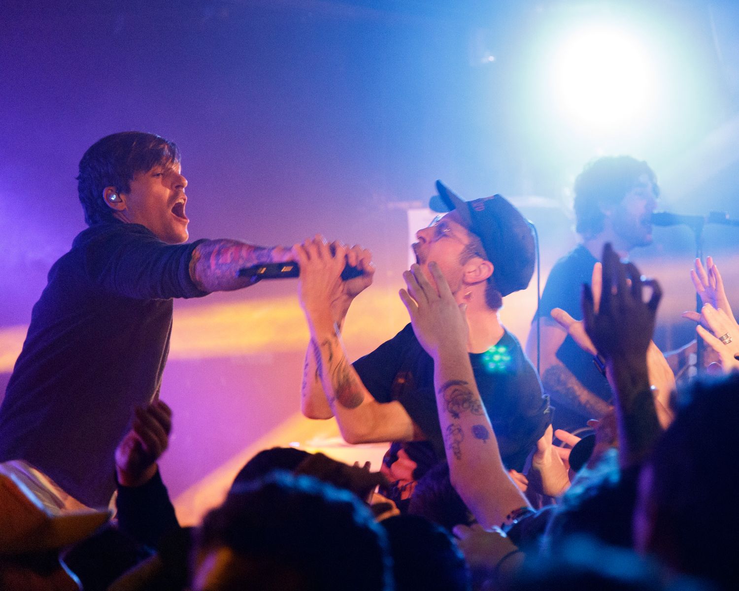 Concert audience silhouettes with raised hands against bright stage lighting effects.