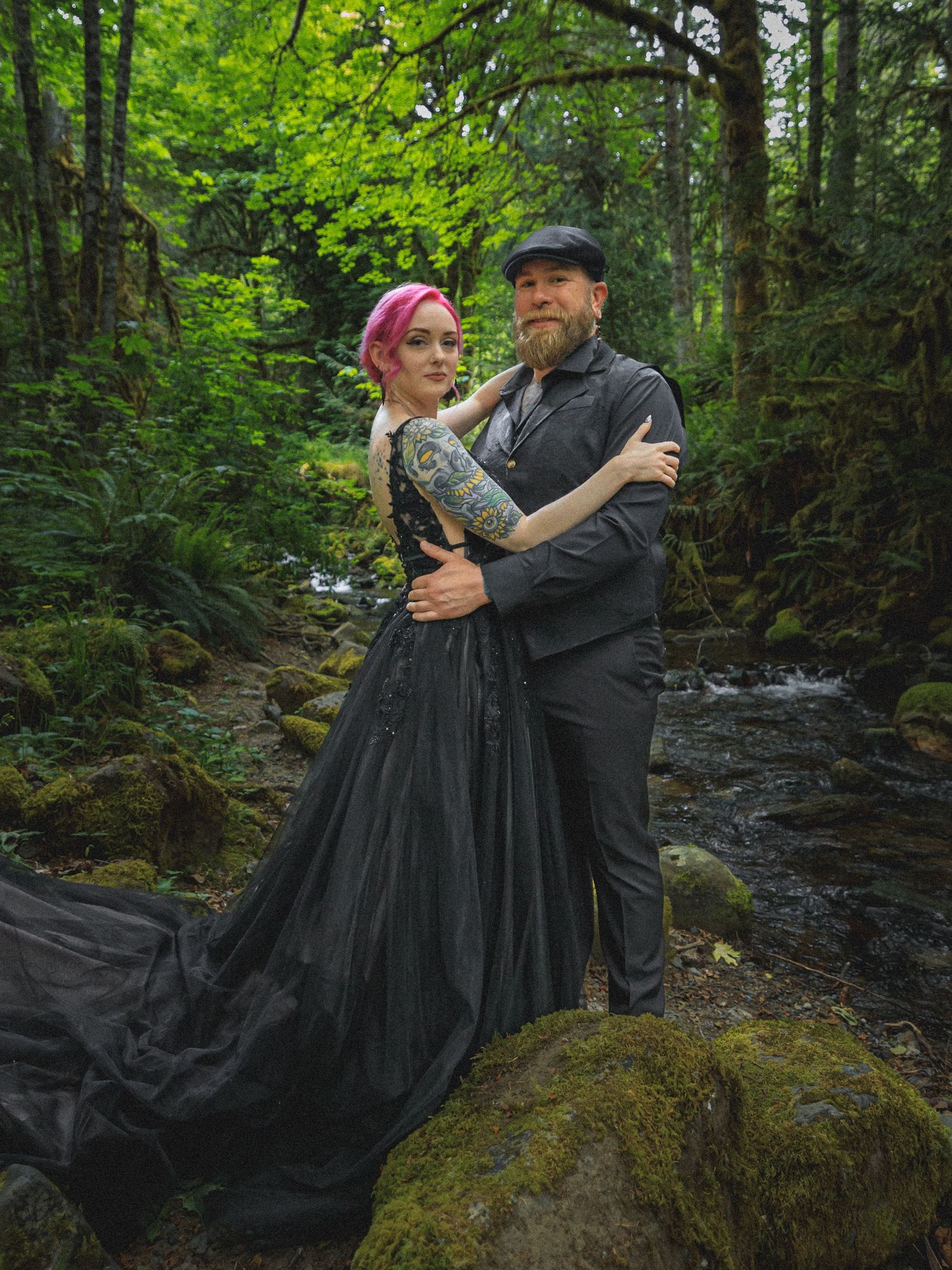 Couple in vintage clothing poses romantically in a lush green forest setting.