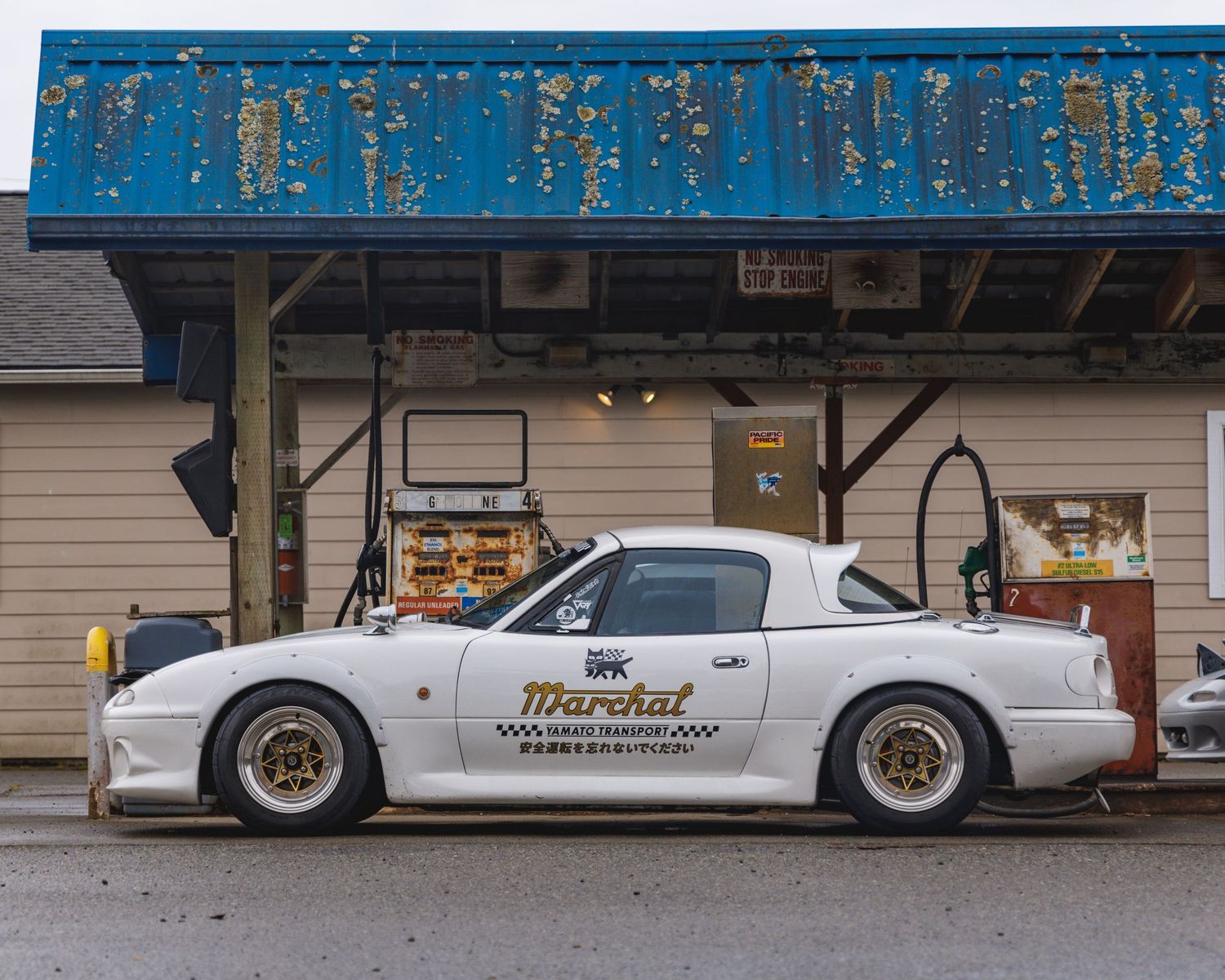 Low angle view of modified sports cars parked in front of a blue industrial building.