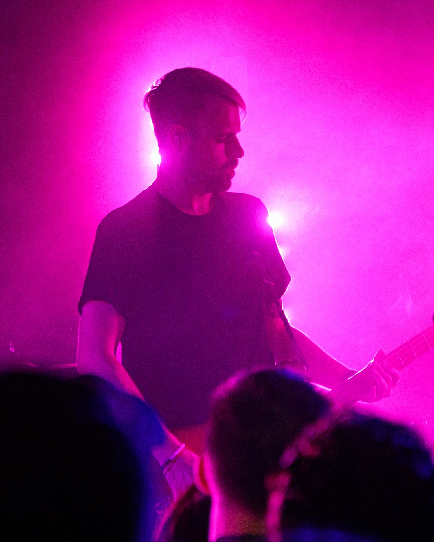 Silhouetted performers on stage bathed in vibrant pink and purple lighting during a live show.