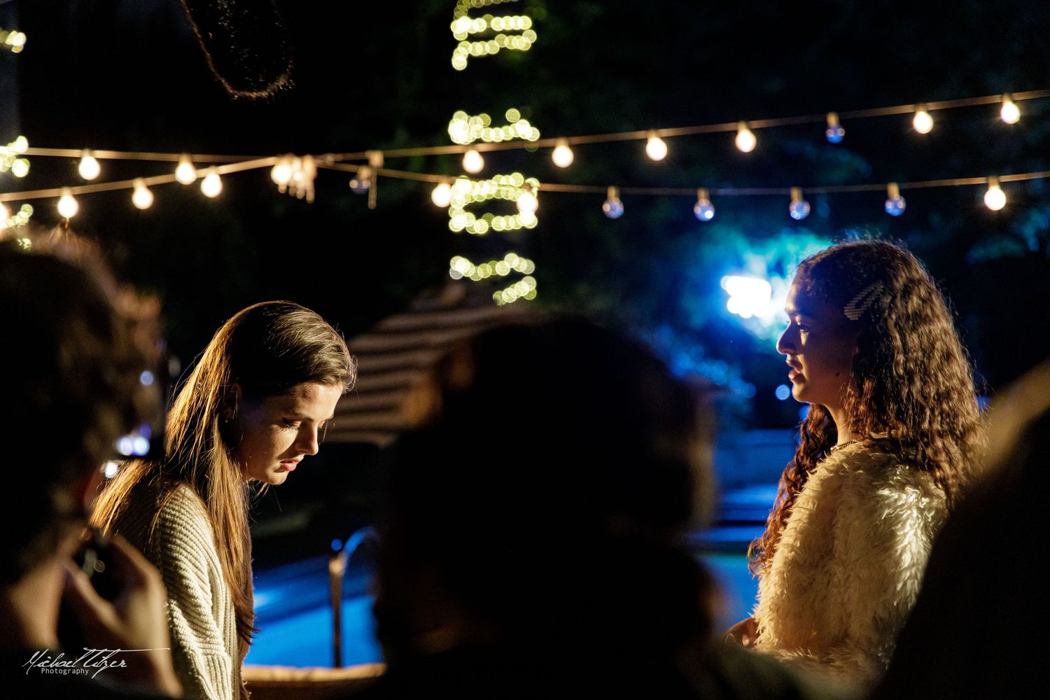 Nighttime film production with string lights creating bokeh effect in background.