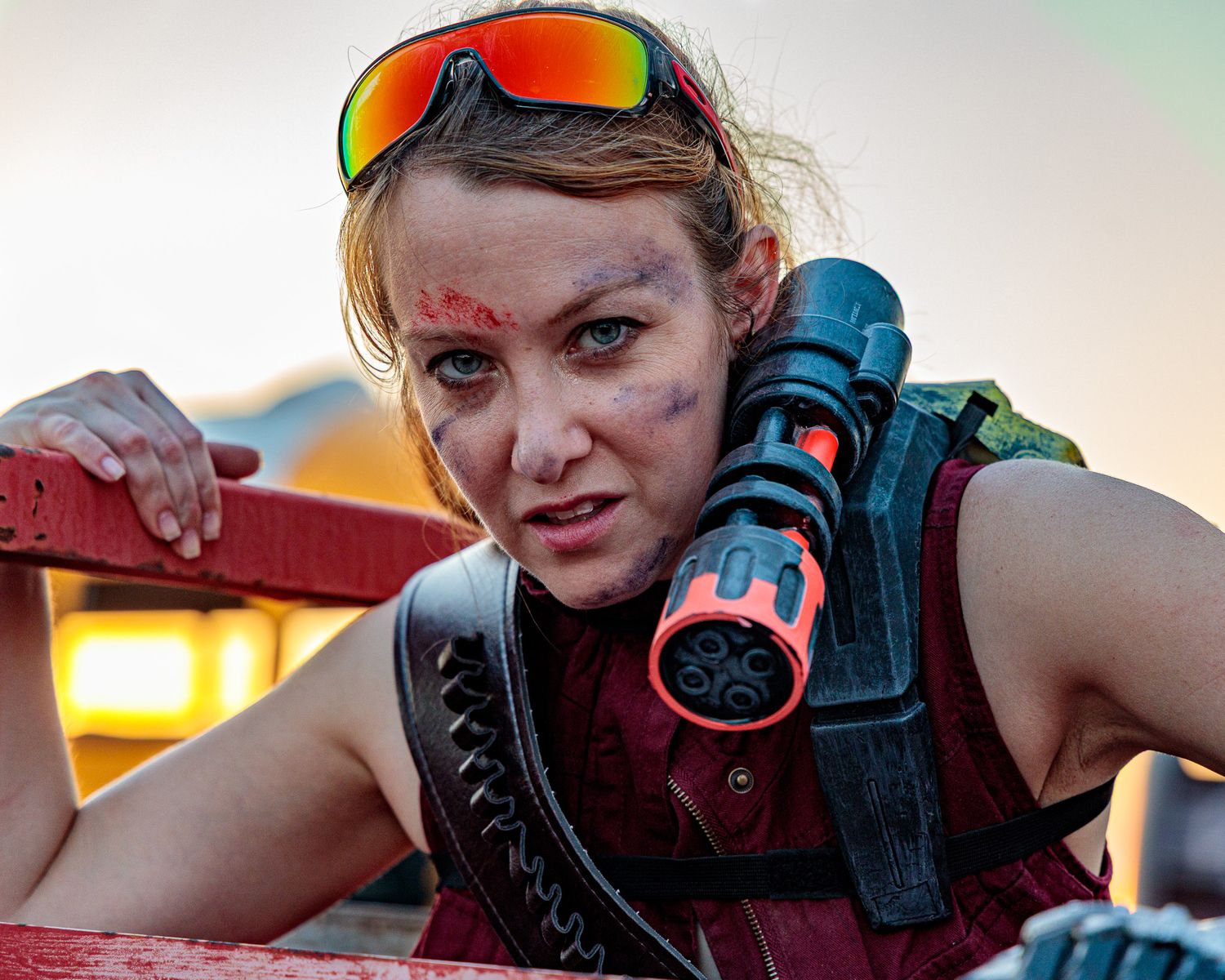 A person in post-apocalyptic gear with orange reflective goggles and tactical equipment.