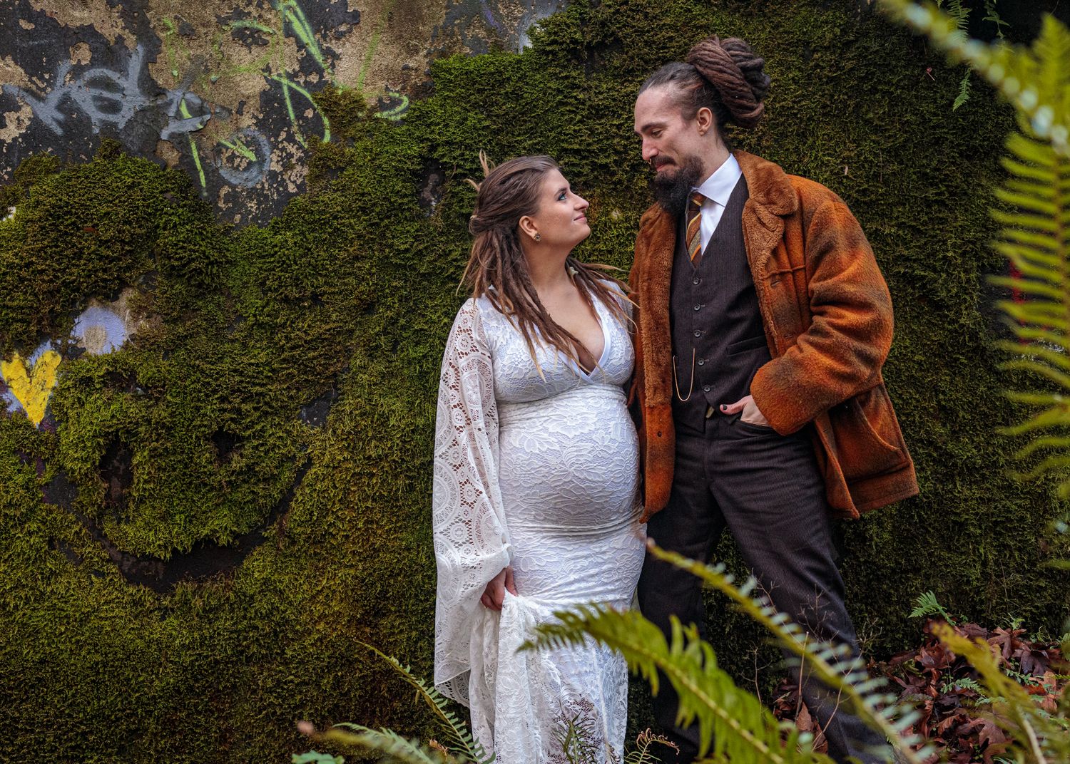 A couple embraces in front of a lush green hedge wall during a romantic photoshoot.