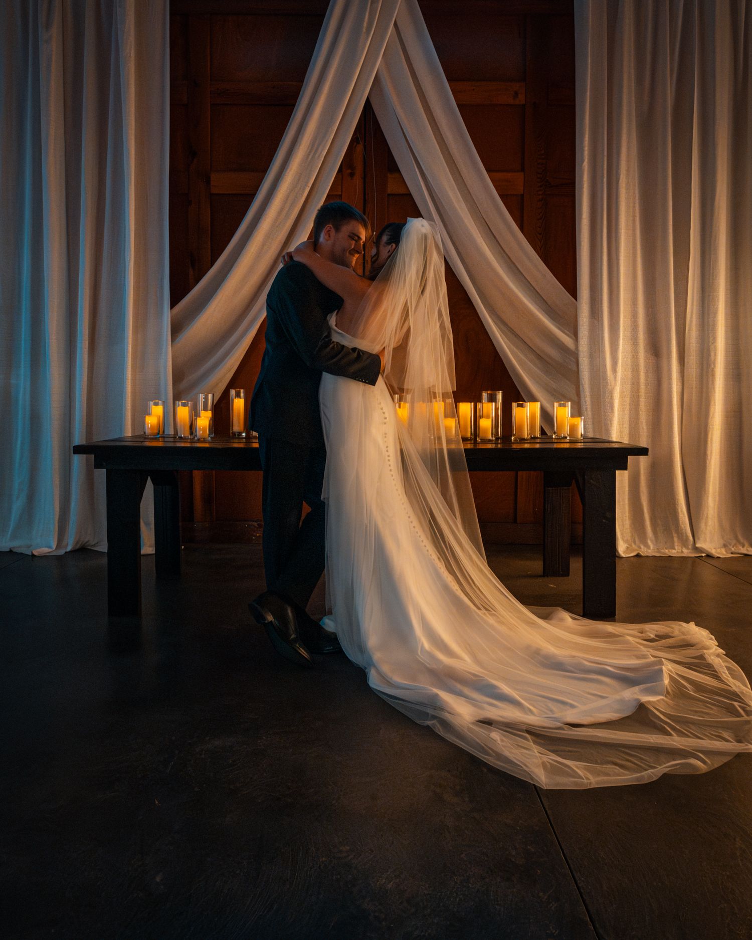 Dramatic low-light wedding photos with flowing white veil and candlelit ambiance.