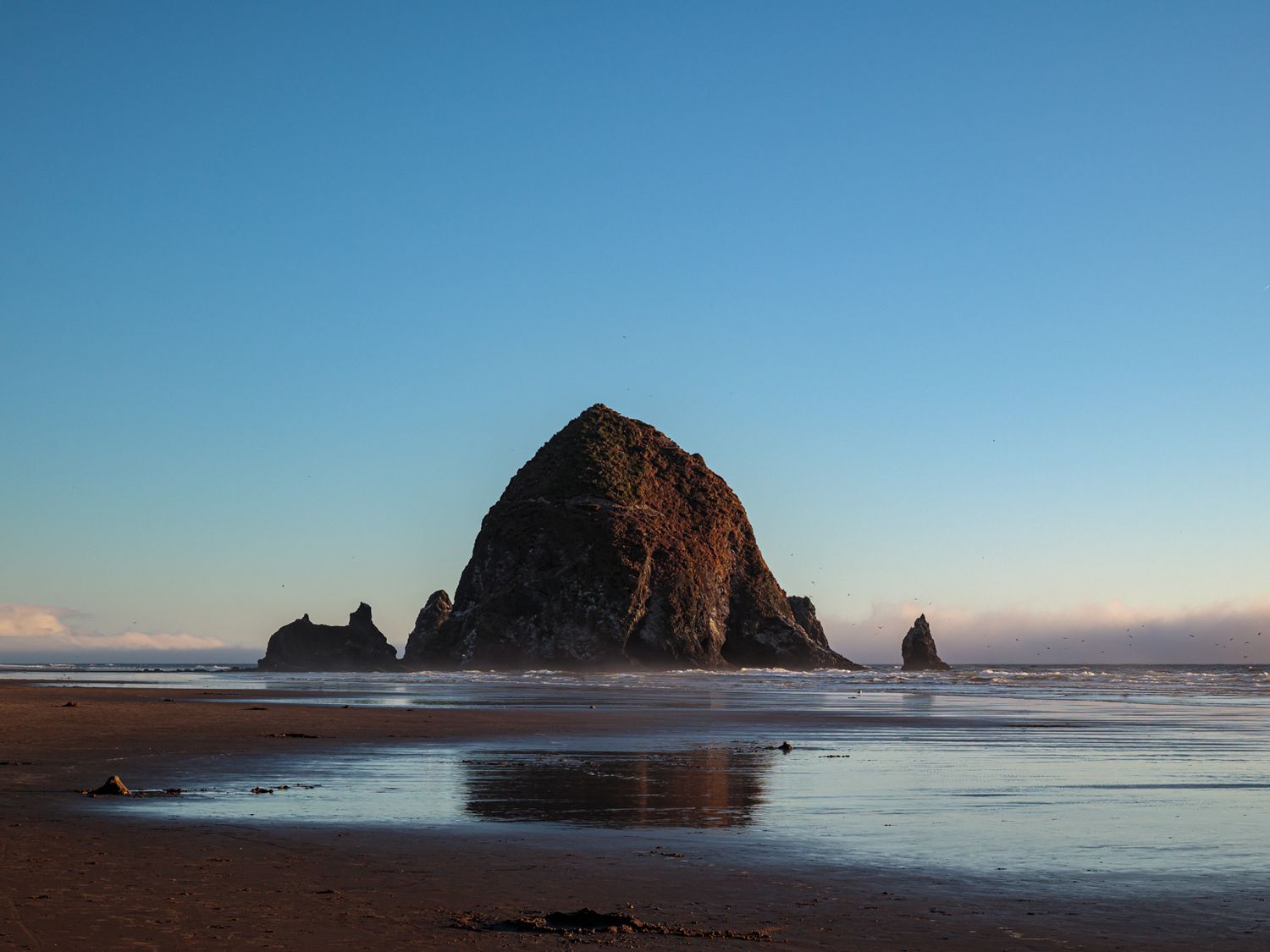 Dramatic coastal landscape with rock formations silhouetted against blue ocean and sky.