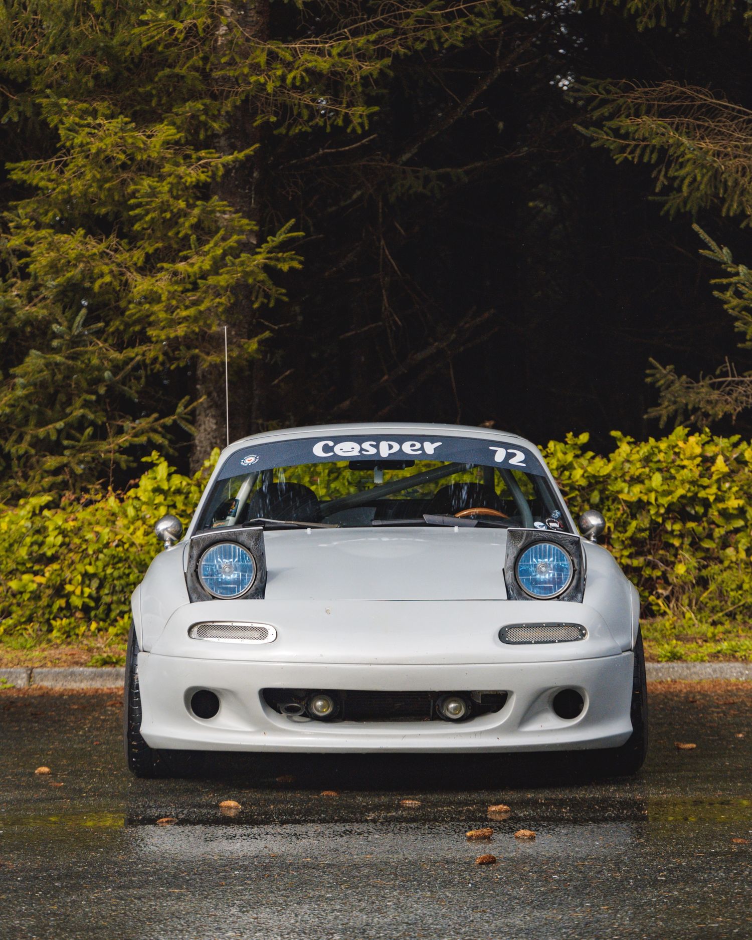 White modified sports car with pop-up headlights and racing stripes photographed at ground level.